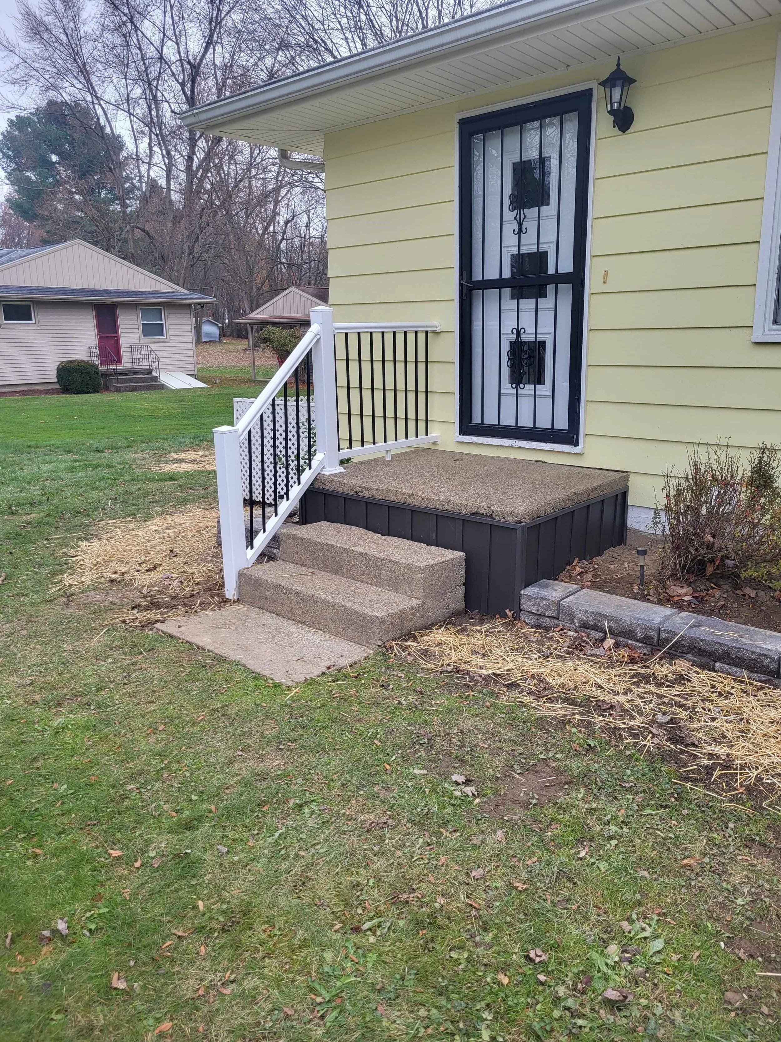 Completed front entrance renovation in Cuyahoga Falls, Ohio featuring restored aggregate concrete steps, dark gray vertical skirting, and a clean white vinyl handrail with black metal balusters by DLR.