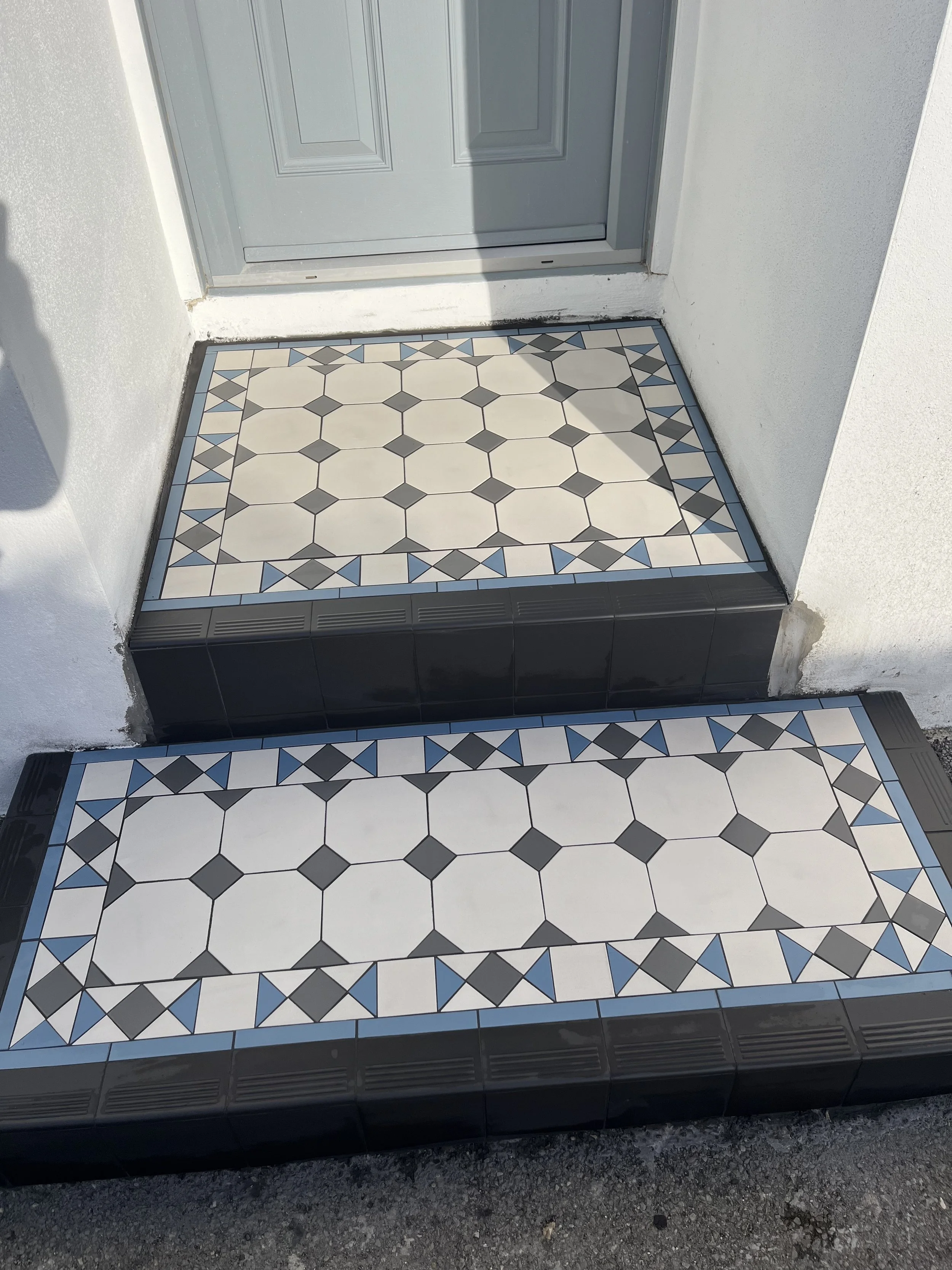 Decorative tiled porch steps with geometric patterns in white, black, gray, and blue surrounding a gray door.