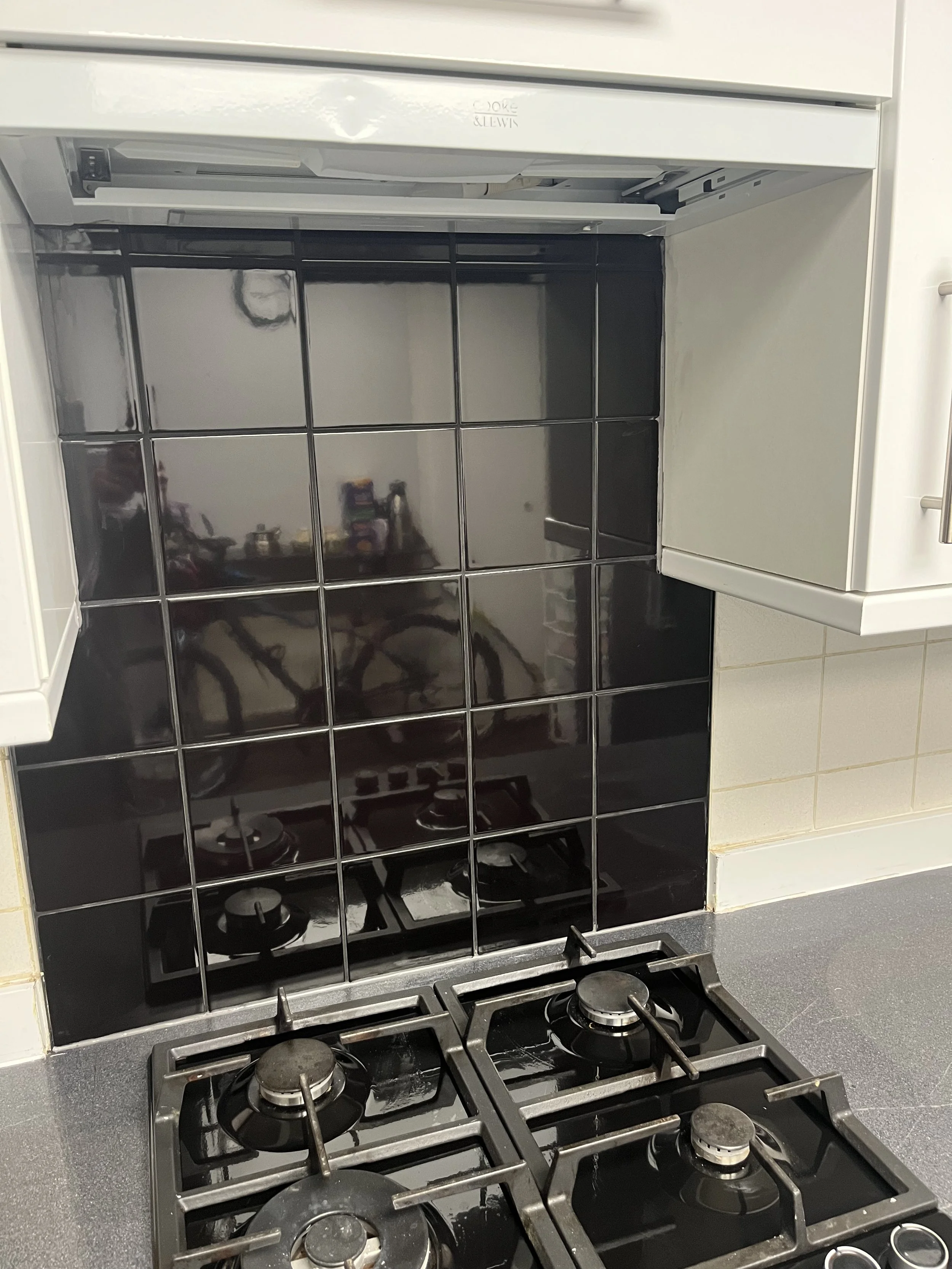 Kitchen stove with four burners, black tiled backsplash, and white cabinets.