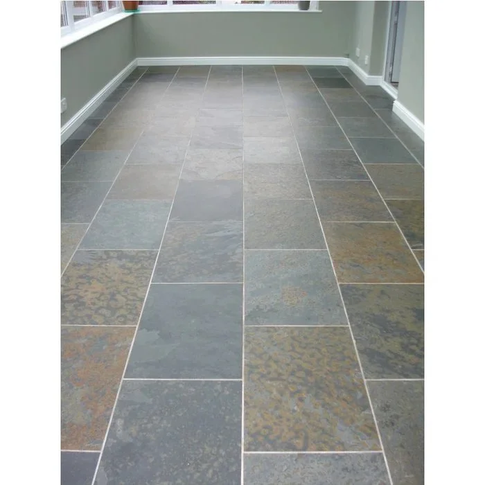 Empty room with large gray and brown stone tile flooring, beige walls, and white baseboards.