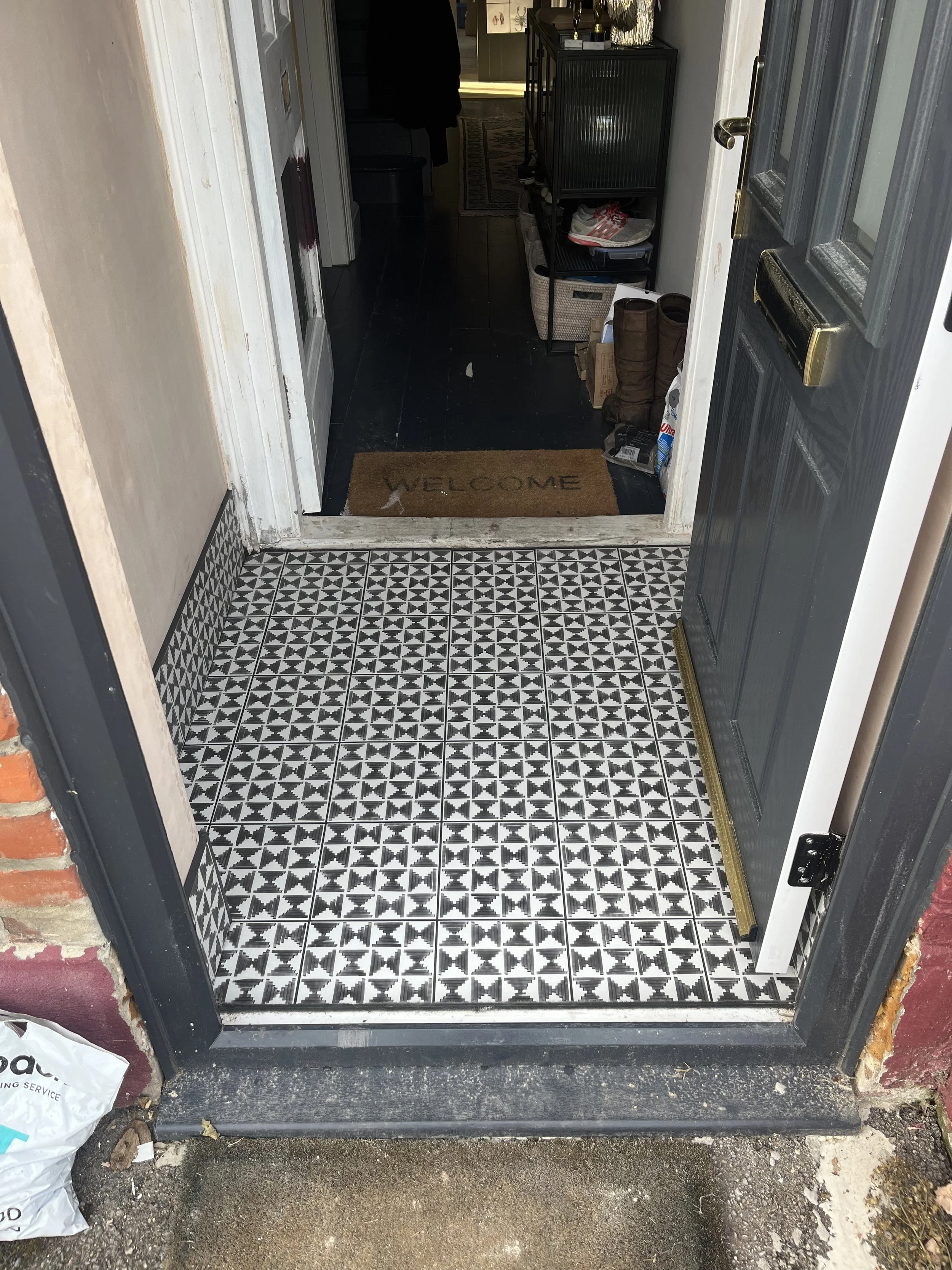 View of a house entryway with black and white patterned tiles, a dark gray door, and a welcome mat inside the room.