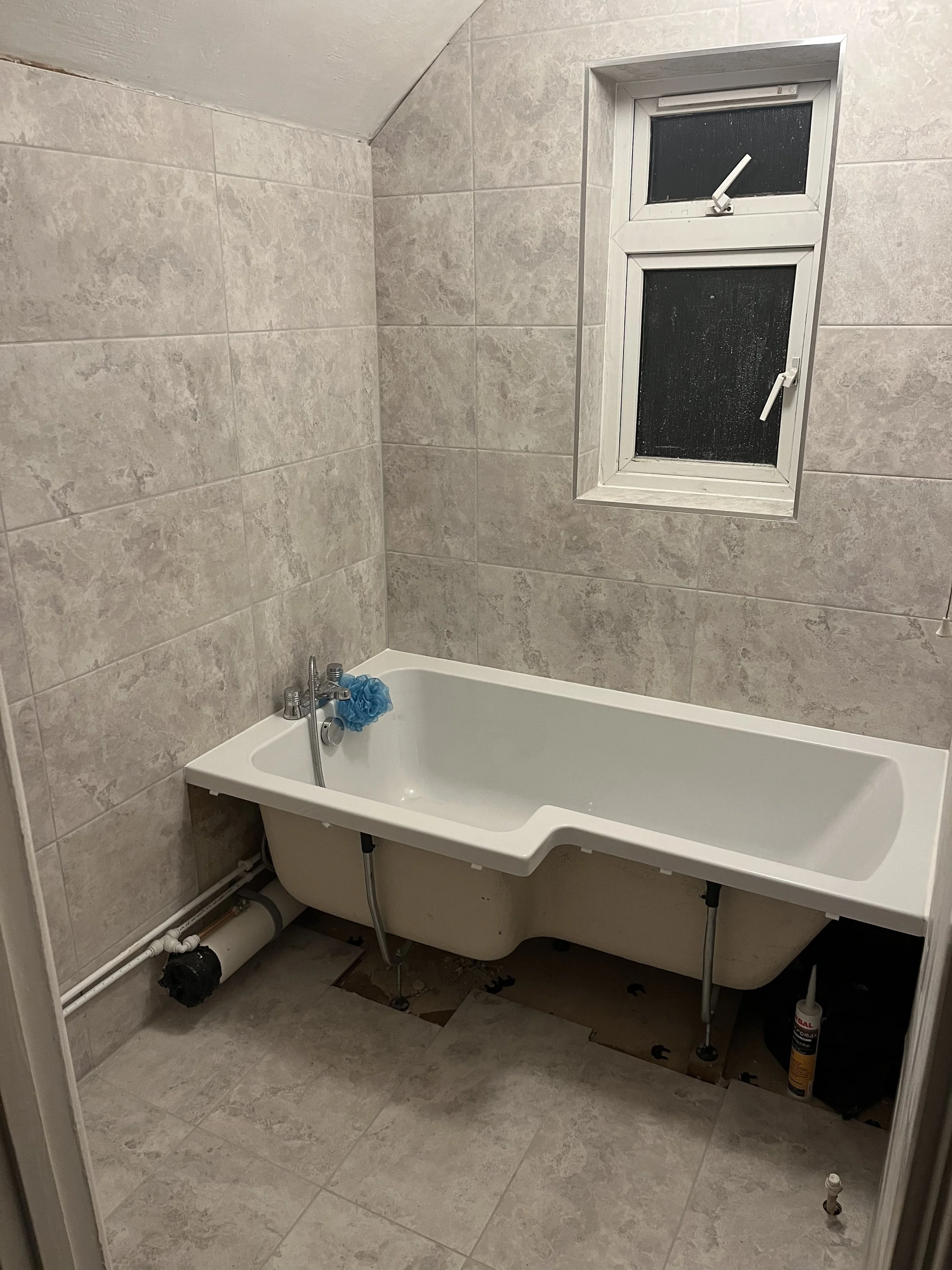 Empty bathroom with partially installed bathtub, gray tiled walls and floors, and a small double-pane window with two open window latches.