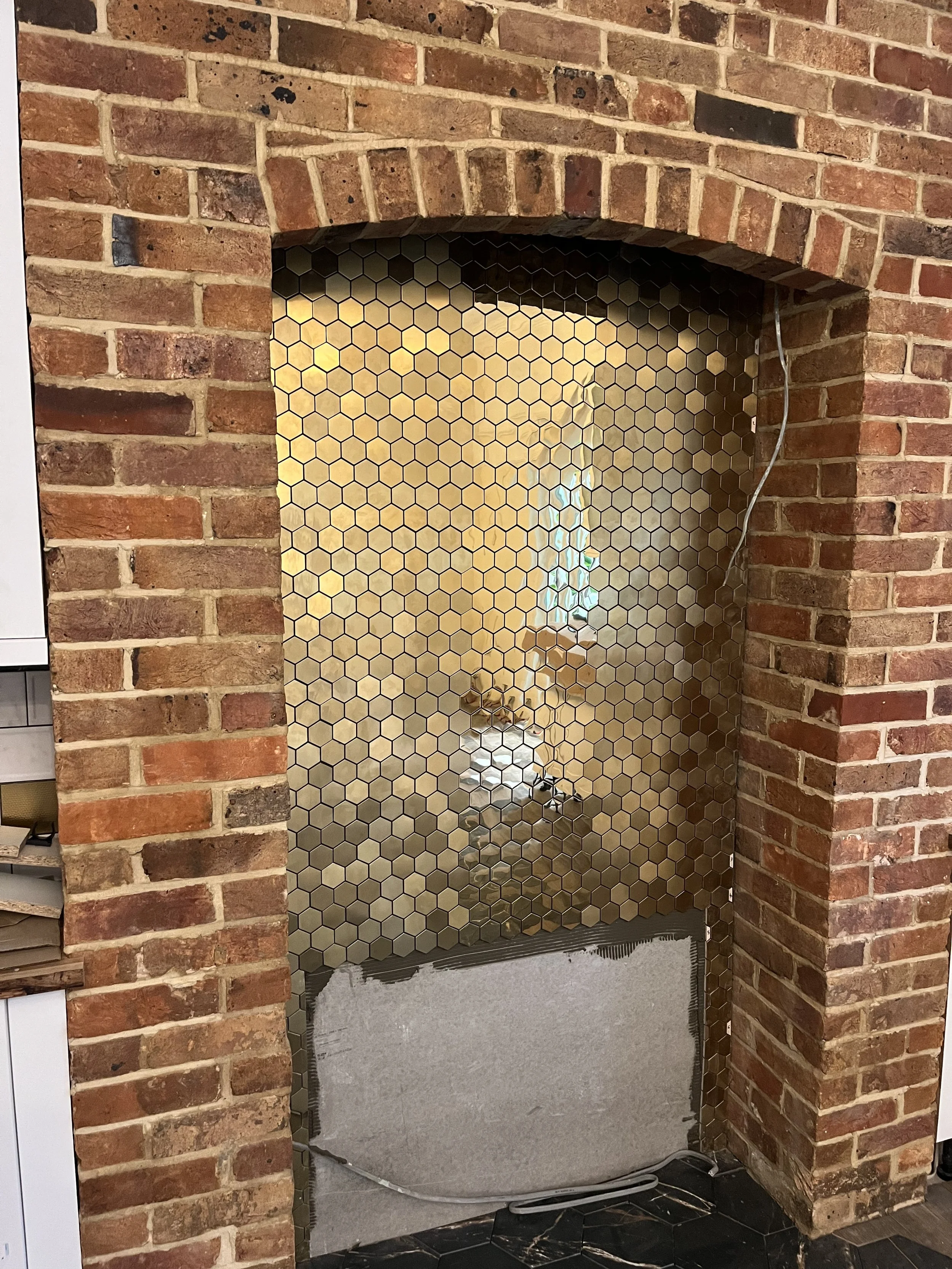 Brick fireplace with a hexagon tile backing, partially renovated with visible wiring and a gray panel at the bottom.