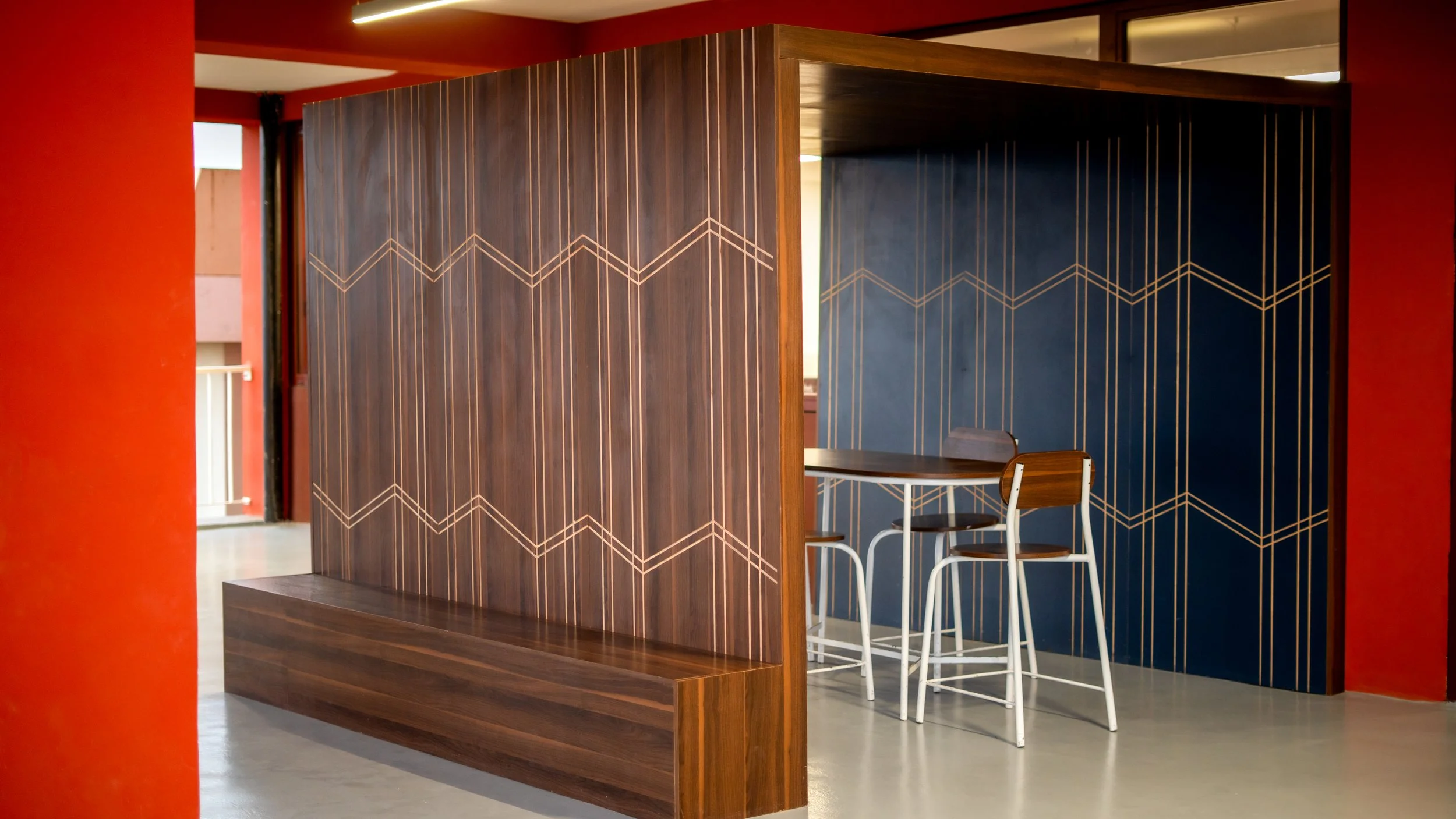 Espace de travail ou zone de réunion avec mur en bois orné de motifs géométriques dorés, tables et chaises en bois et métal, dans un intérieur moderne. sheznou