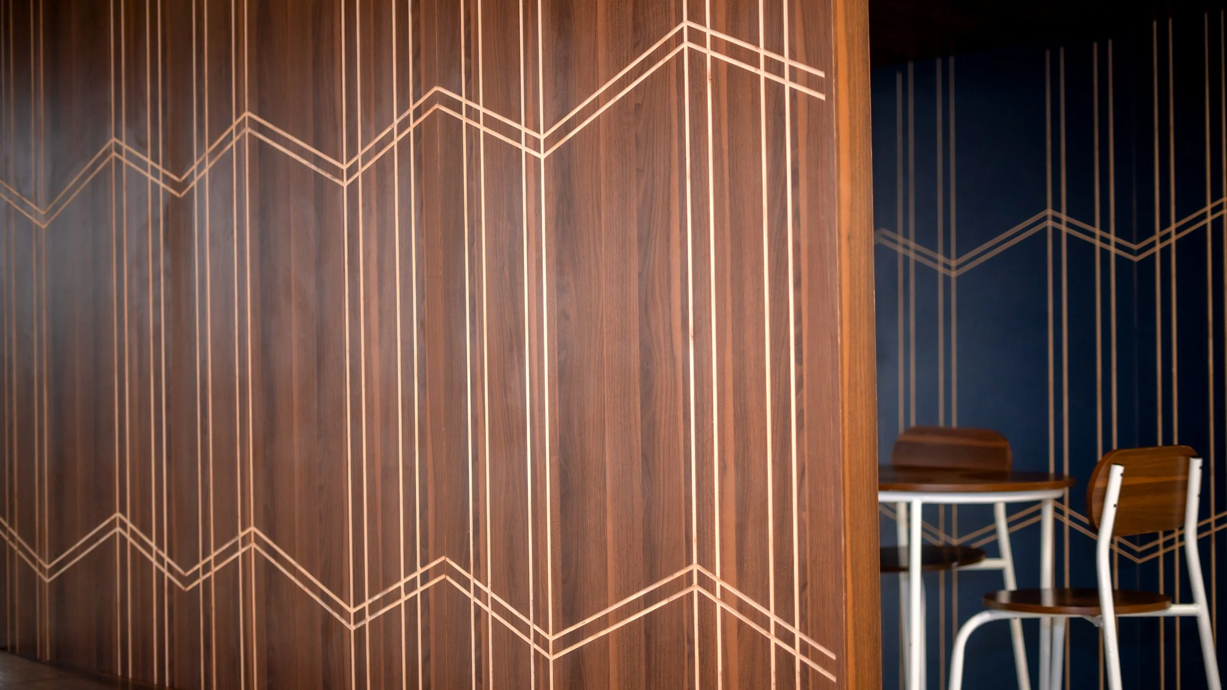 Coin salon avec murs en bois et motifs géométriques dorés, tables et chaises en bois. sheznou