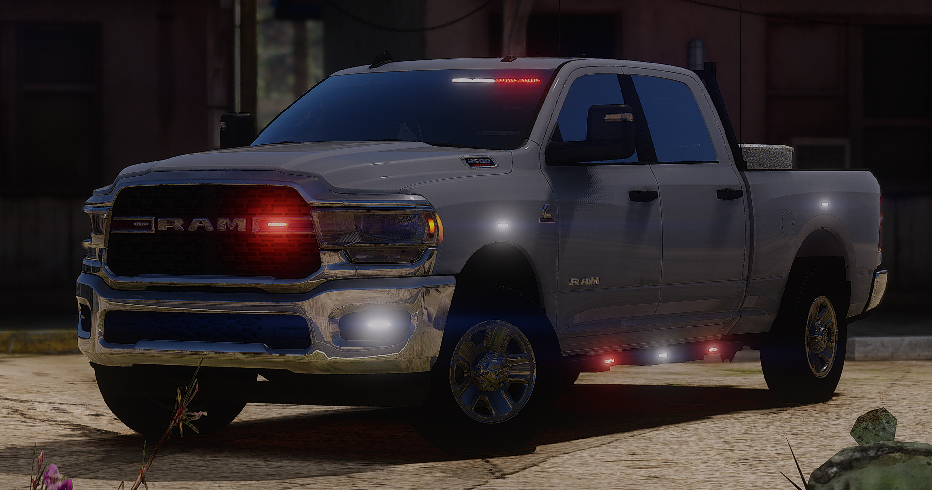 A silver RAM pickup truck with illuminated lights parked outdoors on a paved surface during dusk or dawn.