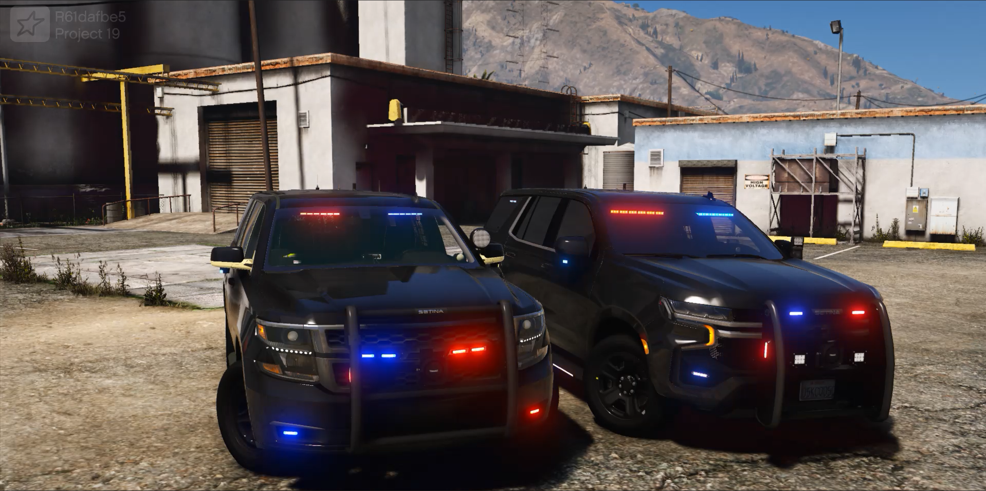 Two police SUVs with emergency lights on parked in front of a building with mountains in the background.