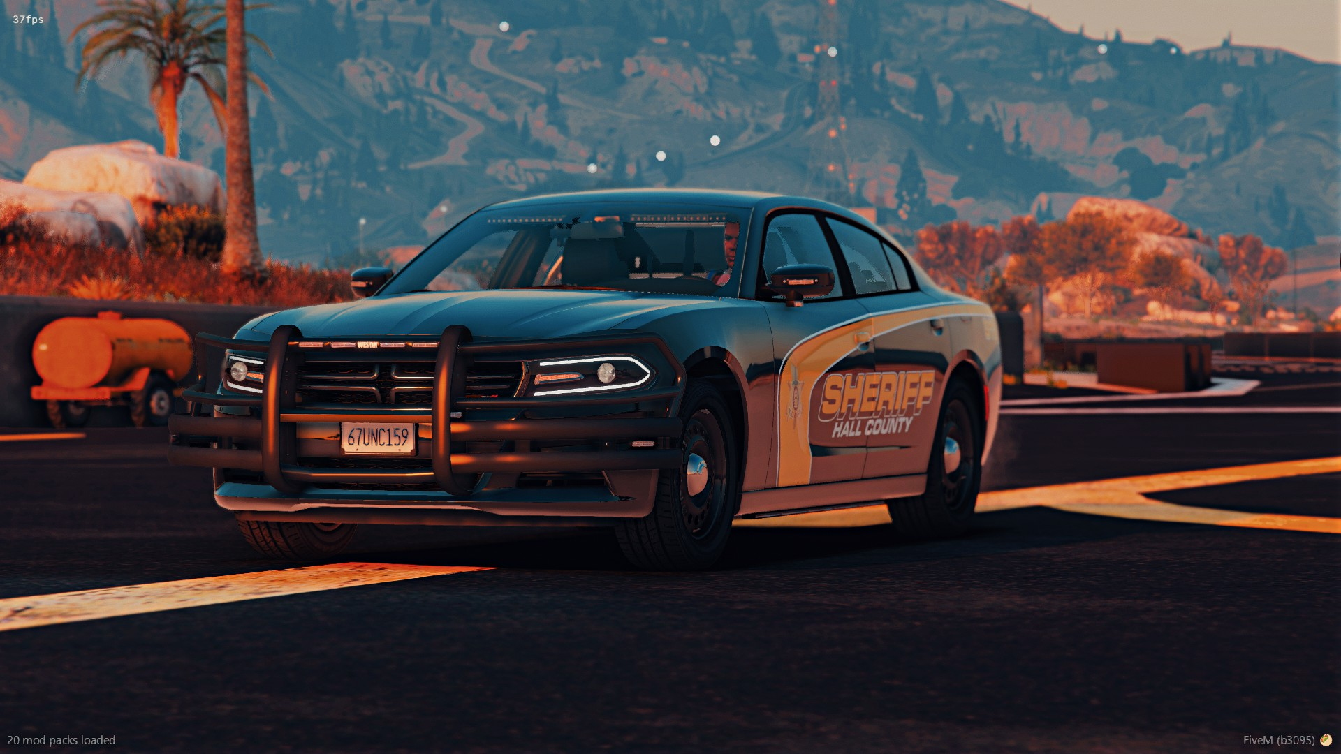 A sheriff's patrol car with Hall County markings parked on a road during sunset with hills and trees in the background.