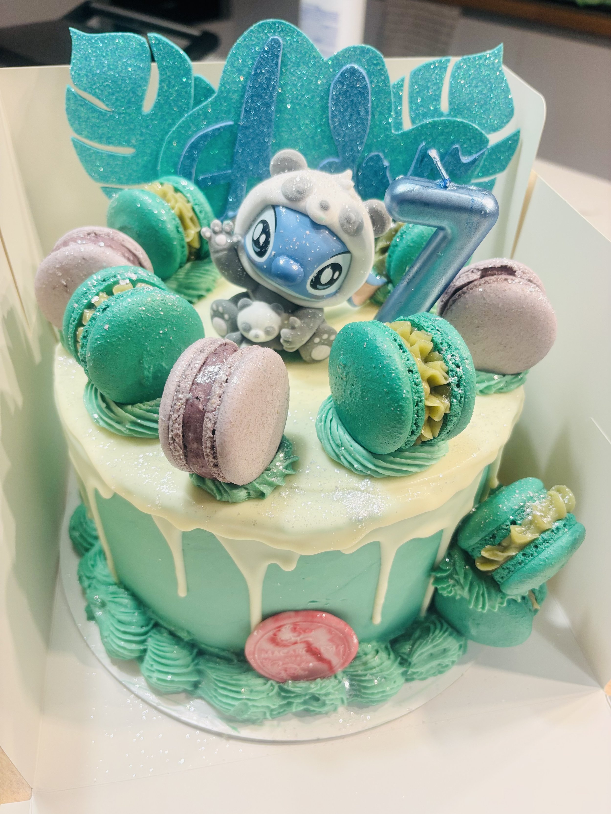 Pastel de cumpleaños decorado con Macarons, una figura de animal y una vela en forma de número 7.