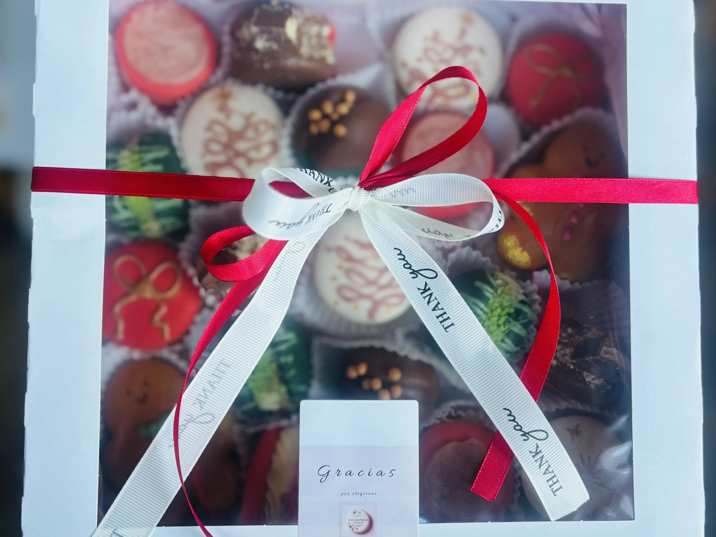 Caja de chocolates decorada con lazo en colores blanco y rojo, con una tarjeta que dice 'Gracias'.