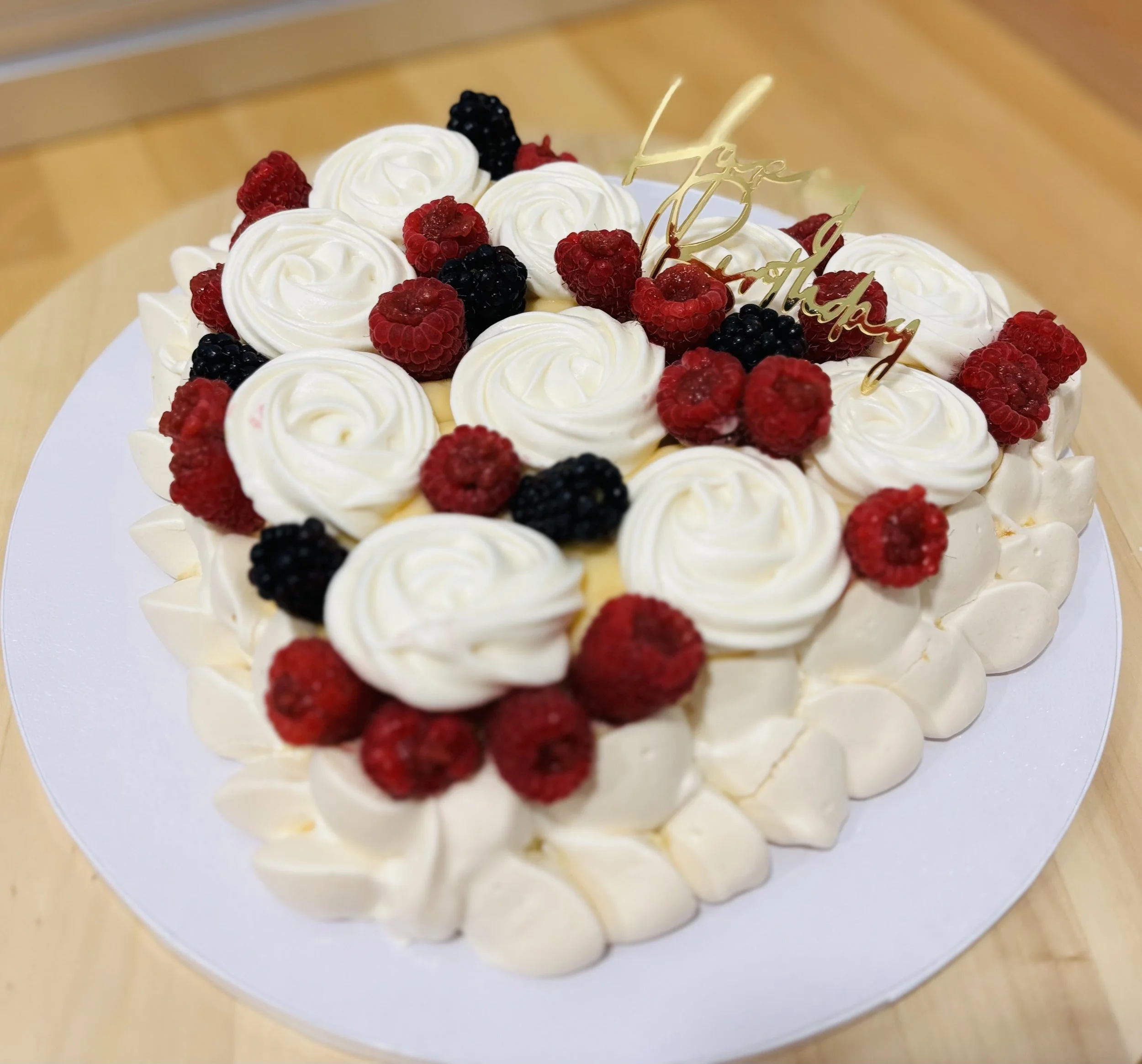 Pastel de bodas con crema y frutos rojos y negros decorativos, con un adorno dorado que dice 'Feliz día'