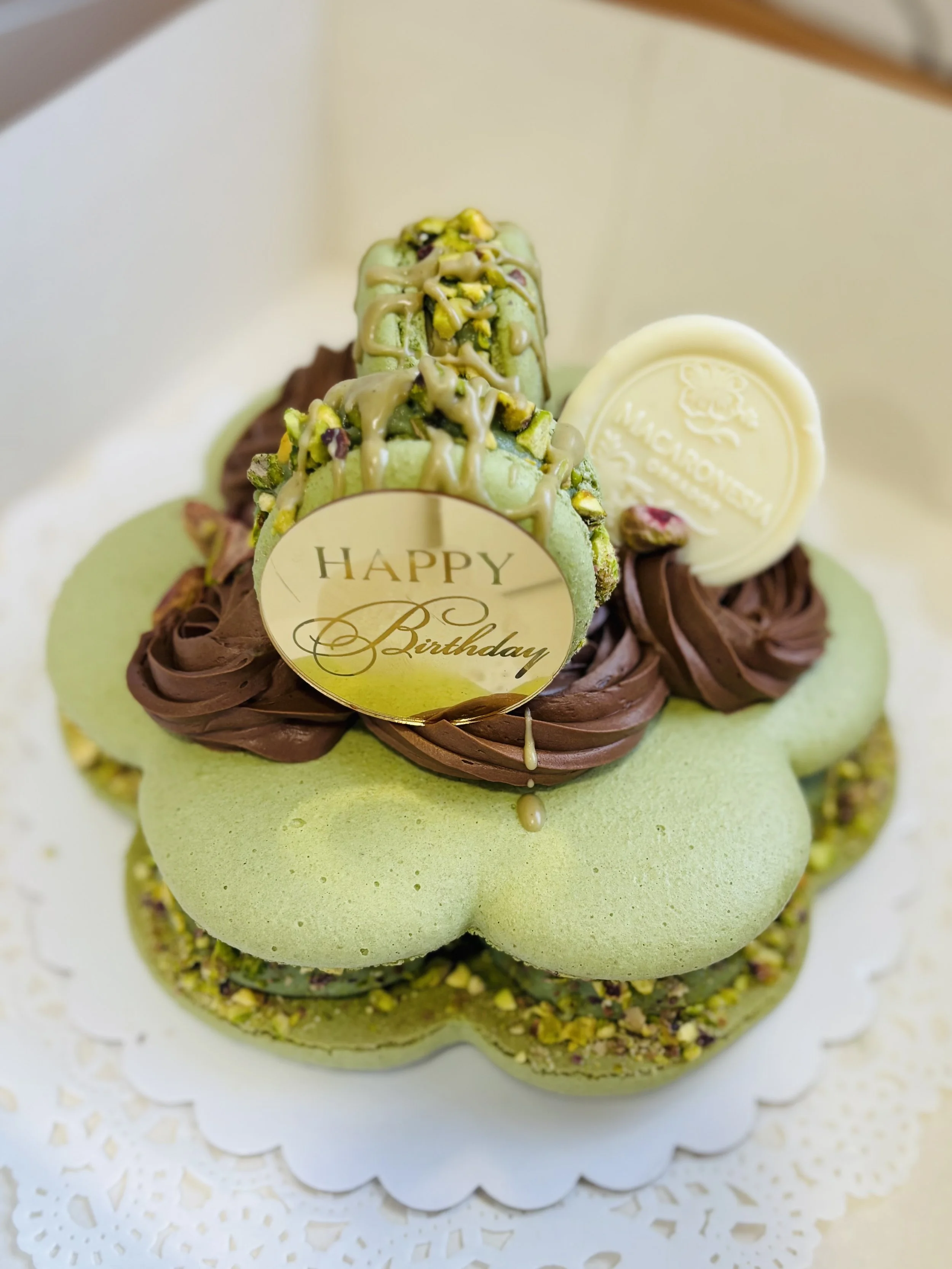 Pastel de cumpleaños con decoraciones de color verde y chocolate, con un mensaje de 'Happy Birthday' y detalles de pistacho.