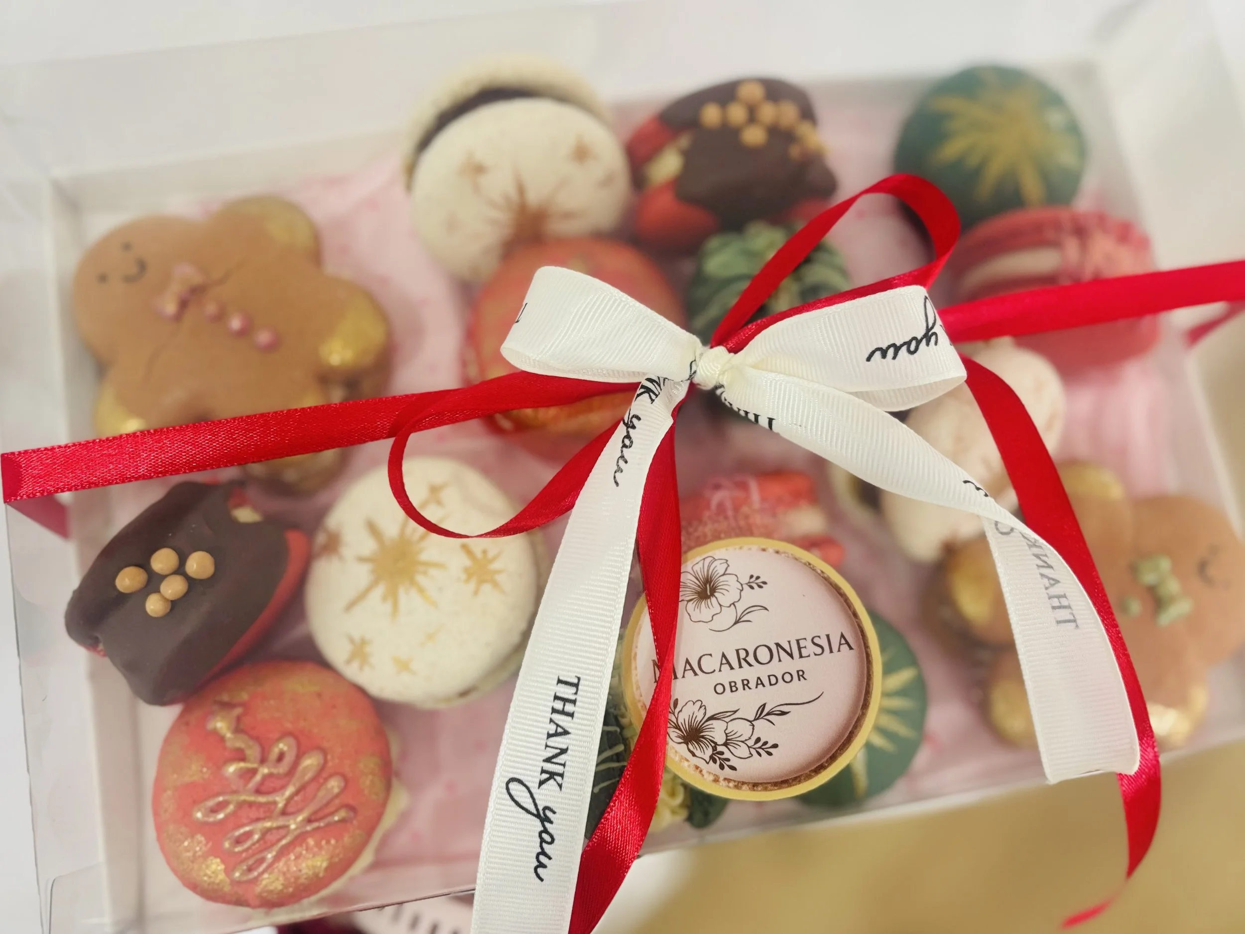 Caja con galletas decoradas con motivos navideños, atadas con lazos rojos y blancos, con una etiqueta que dice "Acaronesia Obrador".