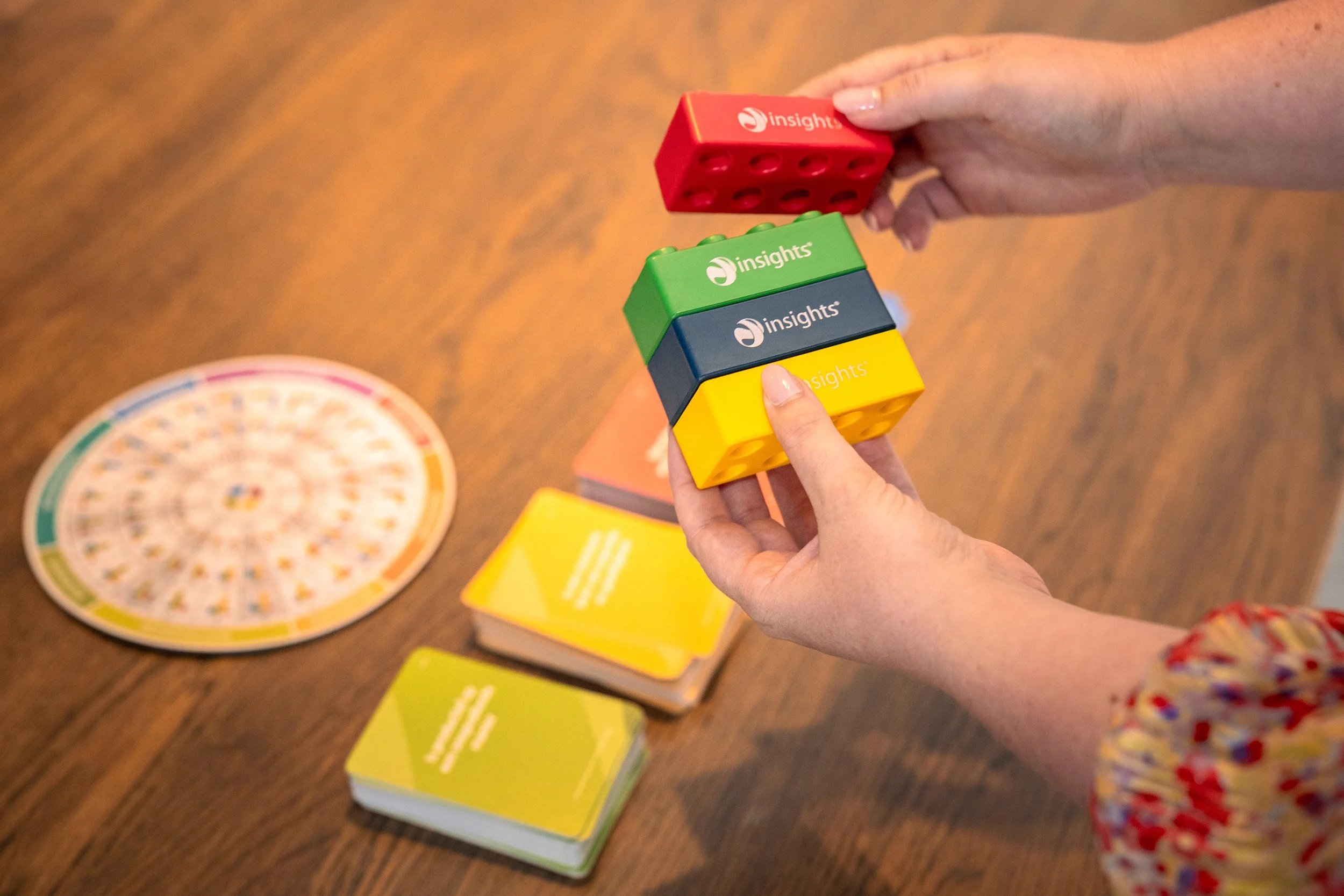 Person die kleurrijke Insight's blokken vasthoudt tijdens een bordspel op een houten tafel.