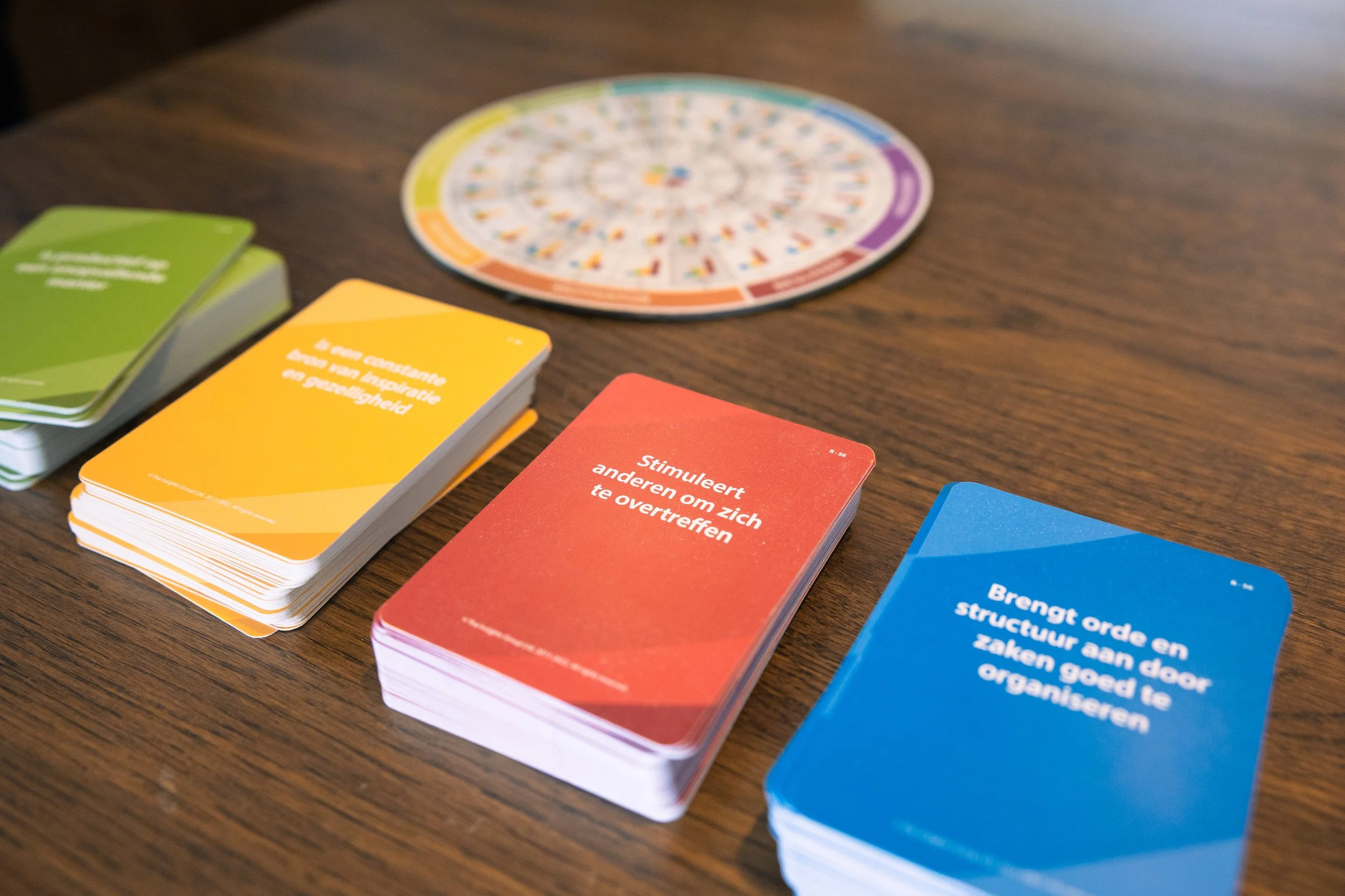 Kaarten voor een spel met verschillende kleuren en tips voor gedrag, naast een cirkel met kleurrijke secties.