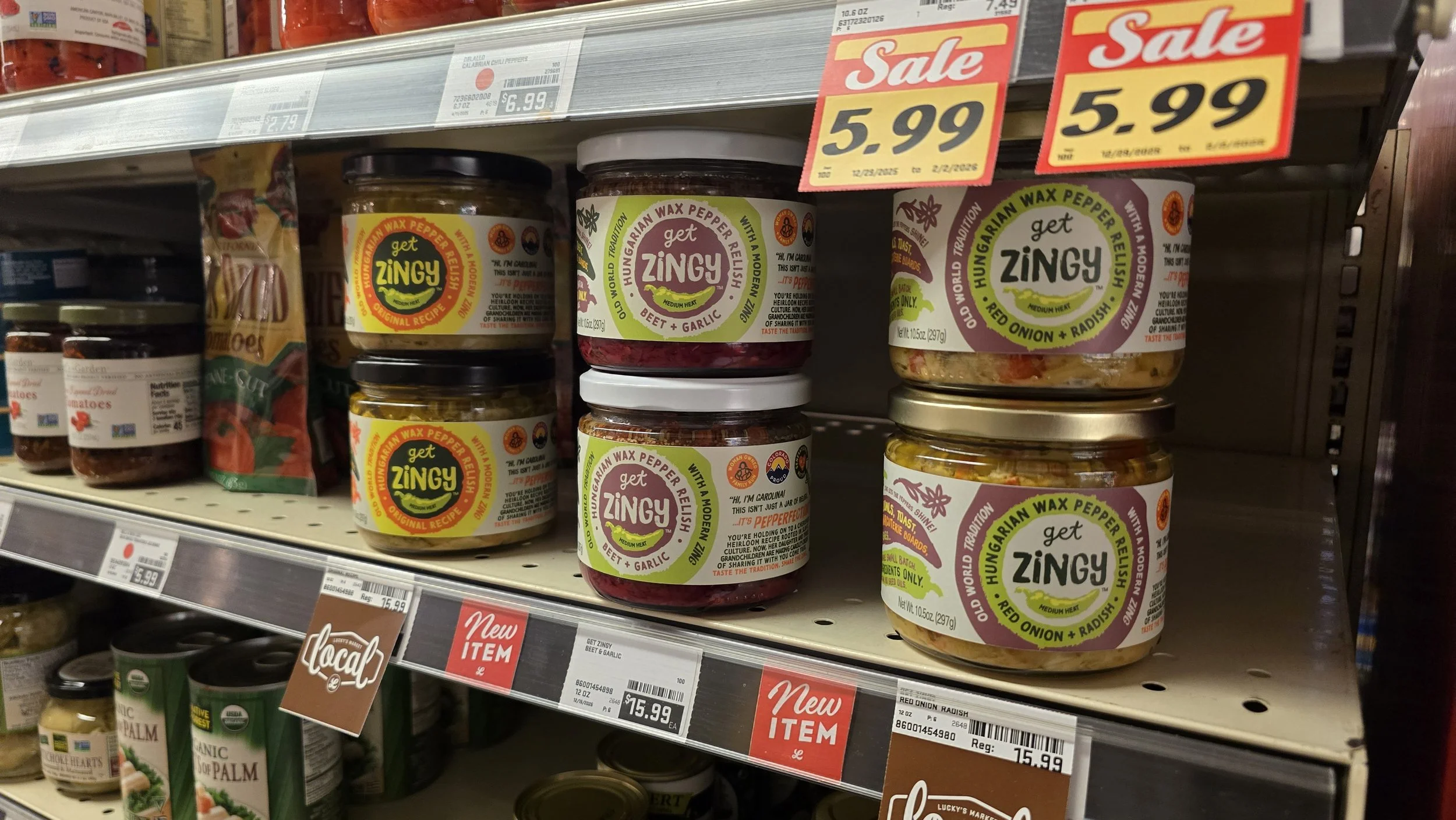 Shelf of jars of Get Zingy Hungarian wax pepper relish with labels showing flavors such as beet and garlic, red onion and radish, and traditional. 
