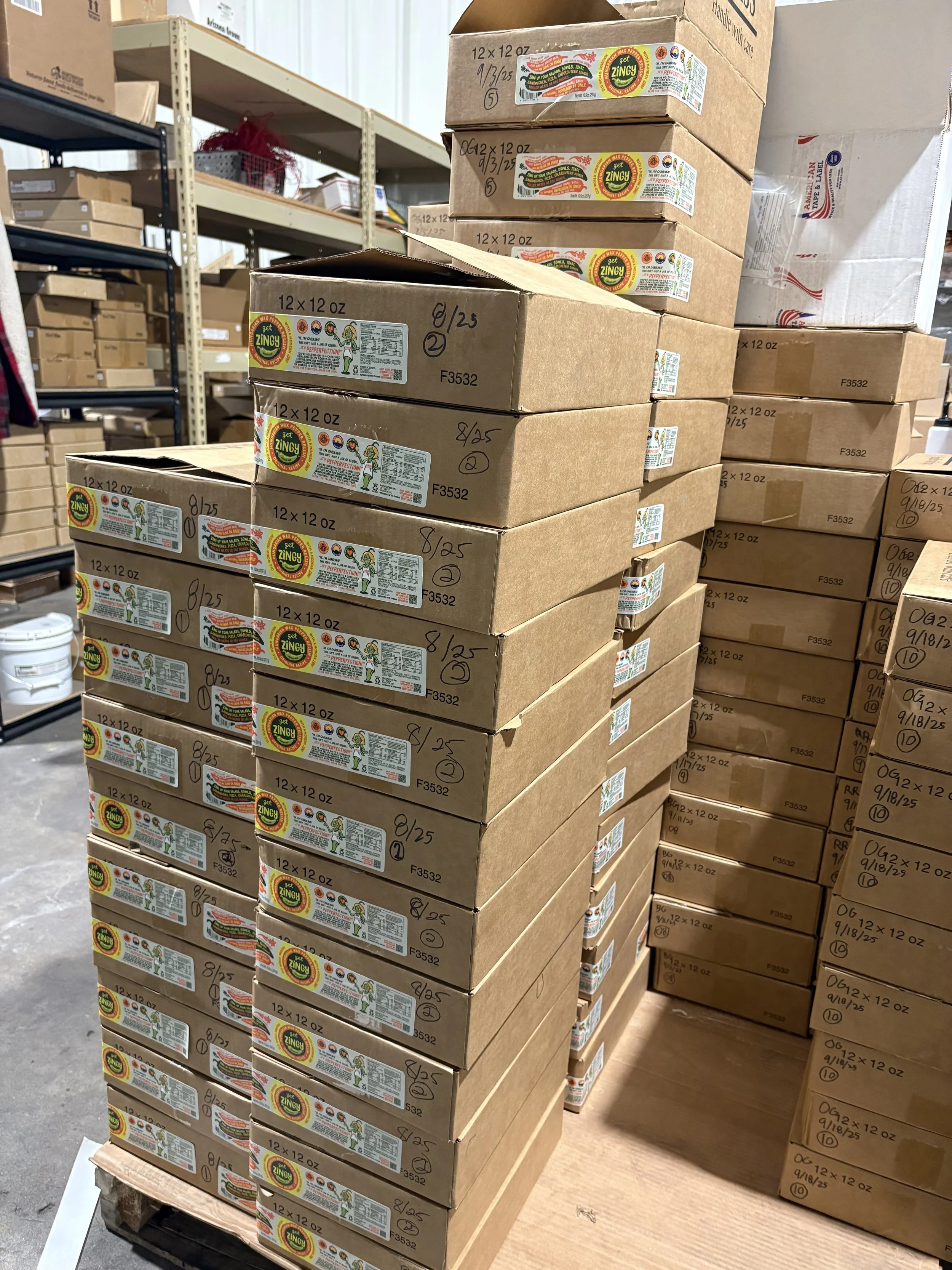 Stacks of cardboard boxes of Get Zingy Hungarian pepper relish on pallets in a warehouse storage area.