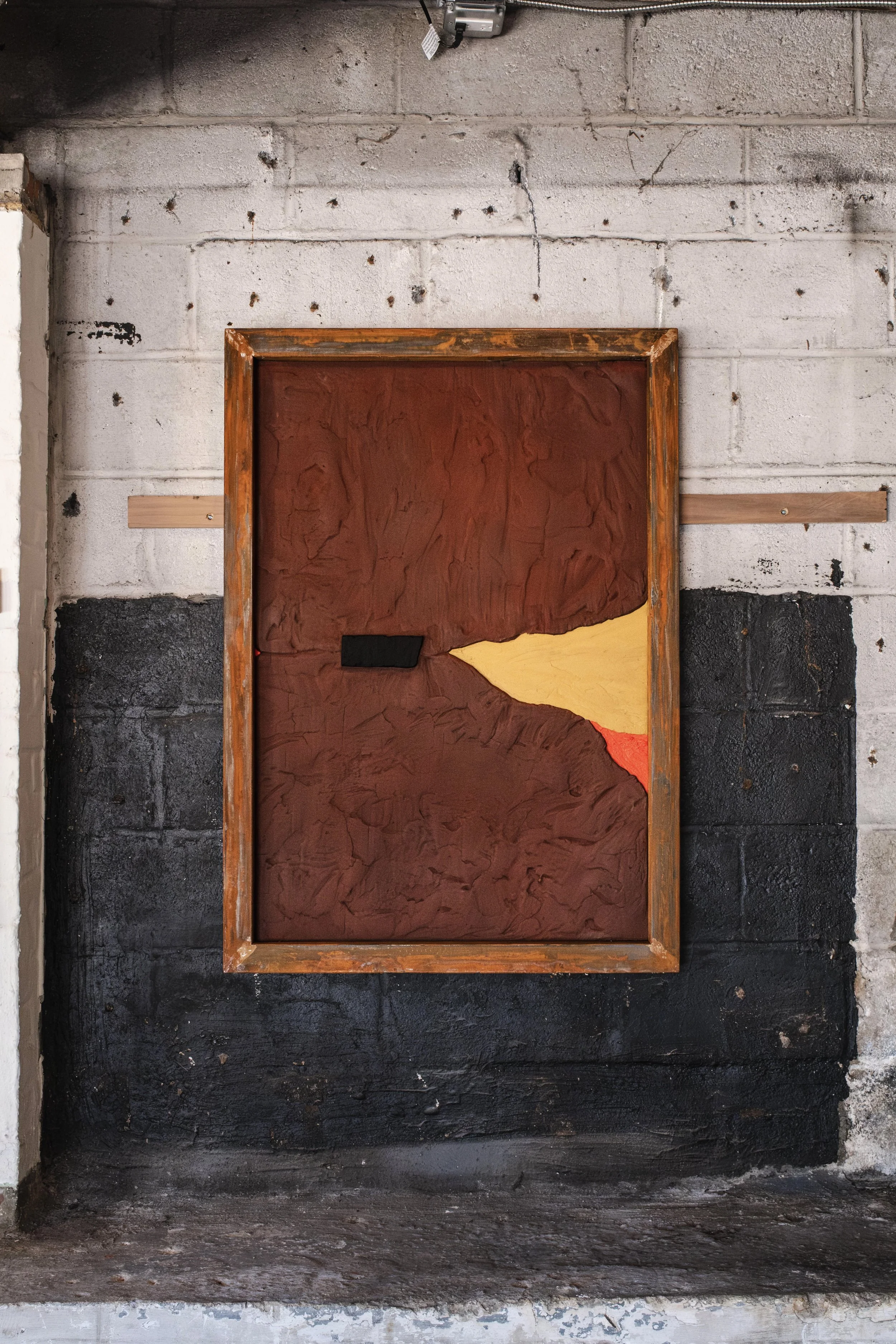 A large sculpted painting, rust, gold, red, and framed in rusted steal hanging on an exposed french cleat.