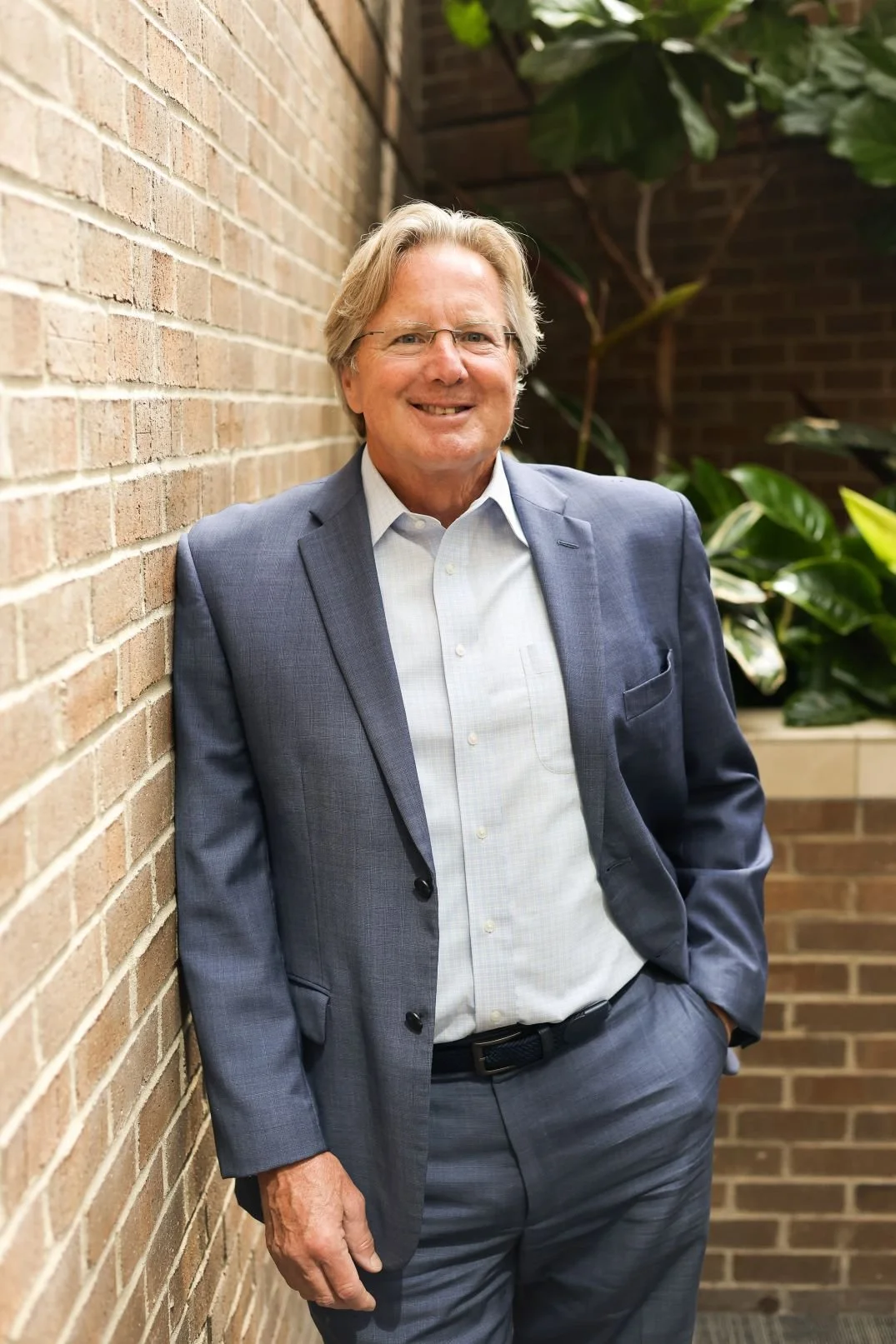 Richard Boucher in grey suit leaning again a wall smiling