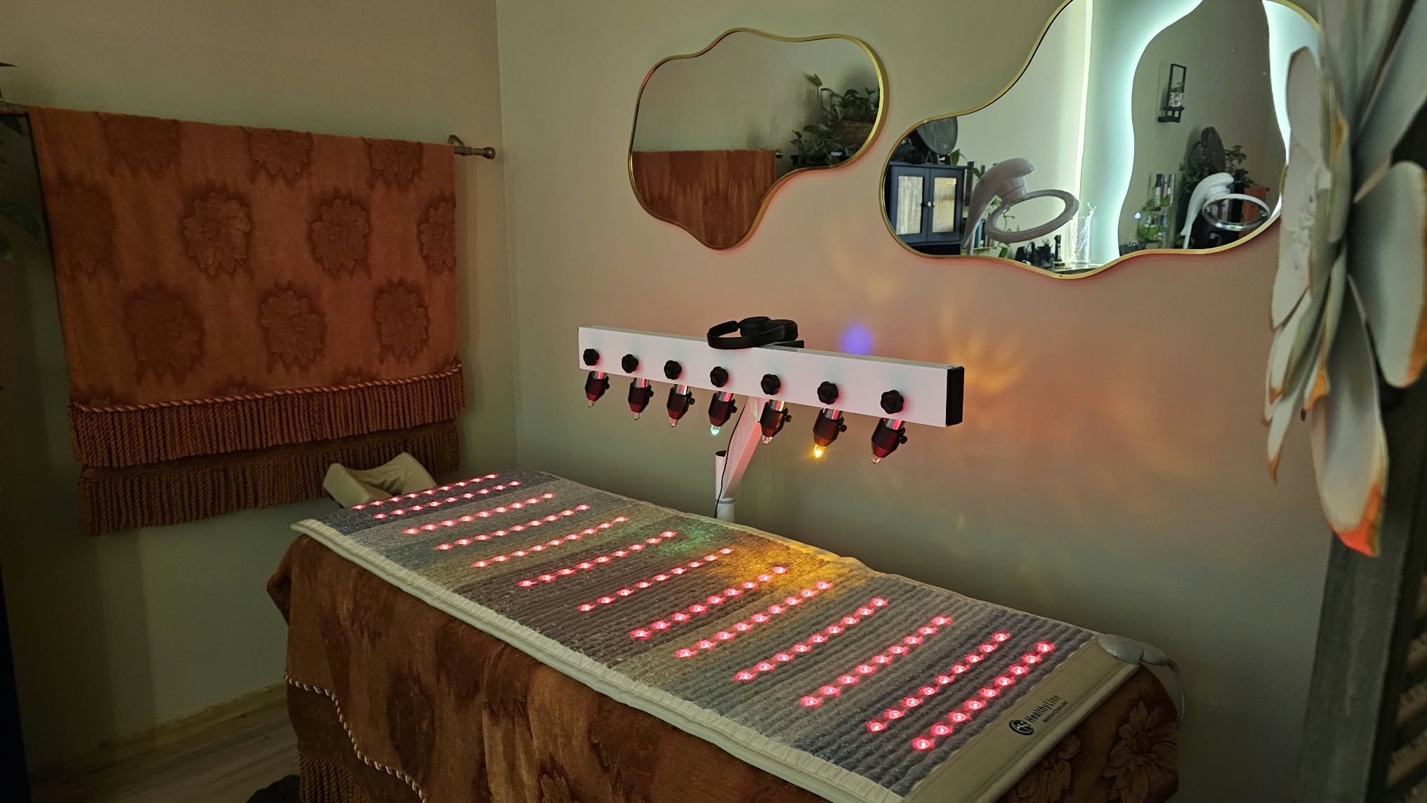 Spa treatment room with a heated therapy mat featuring red LED lights and an overhead infrared light therapy panel
