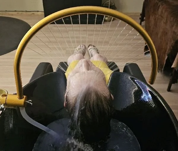 Child seated in a black indoor swing or adaptive chair, viewed from above with feet extended and a yellow safety bar.