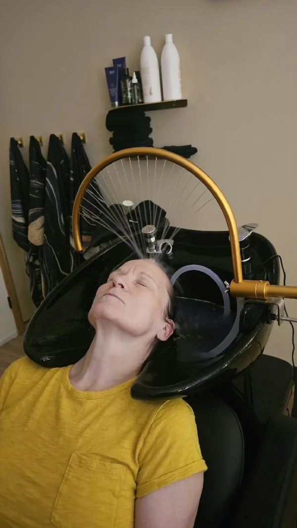 Person reclining at a salon shampoo station while receiving a hair-washing treatment
