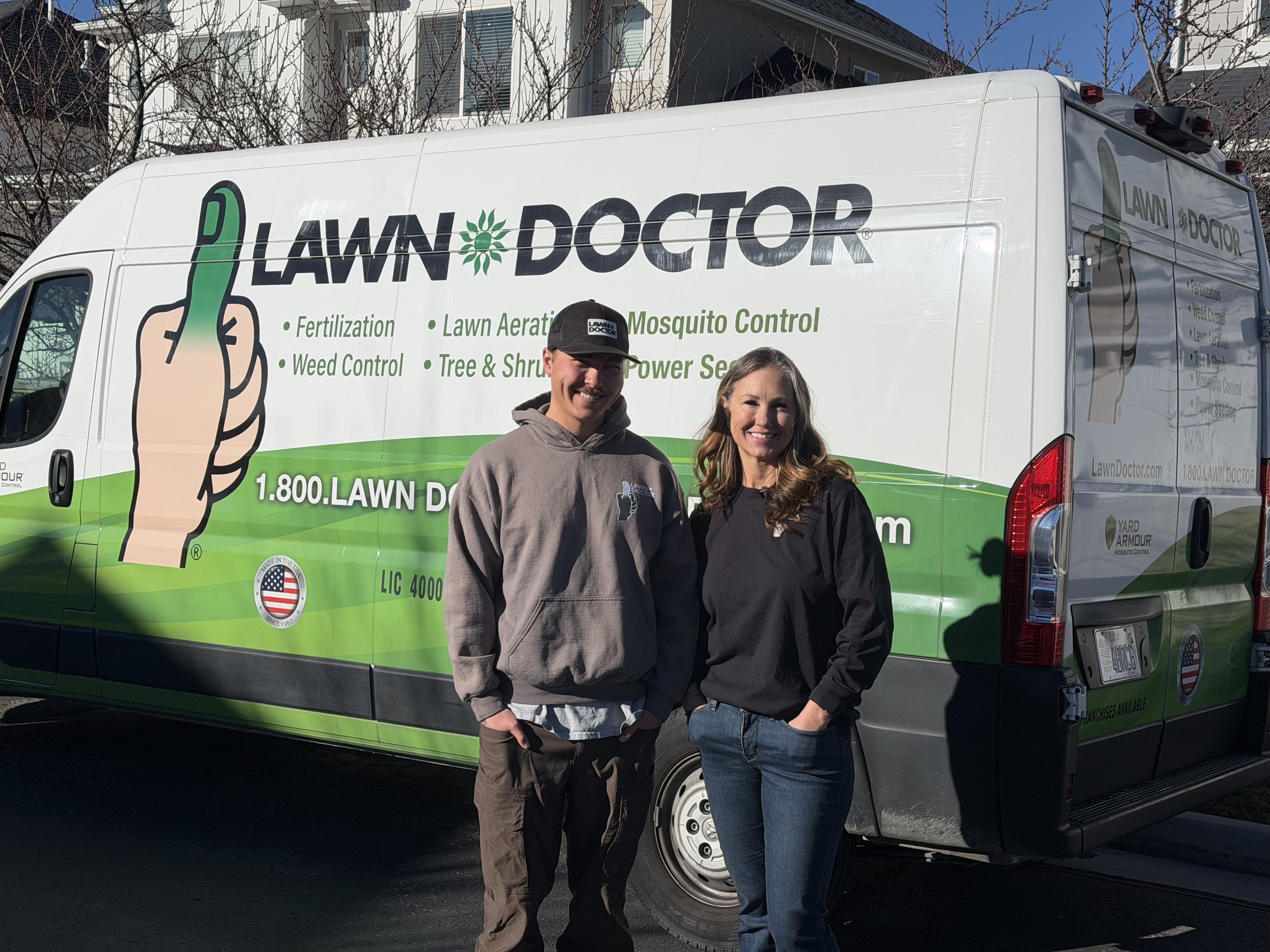 Terra and Ty, the local team behind Lawn Doctor of Utah County & Heber Valley, standing beside their branded lawn care and pest control service van.