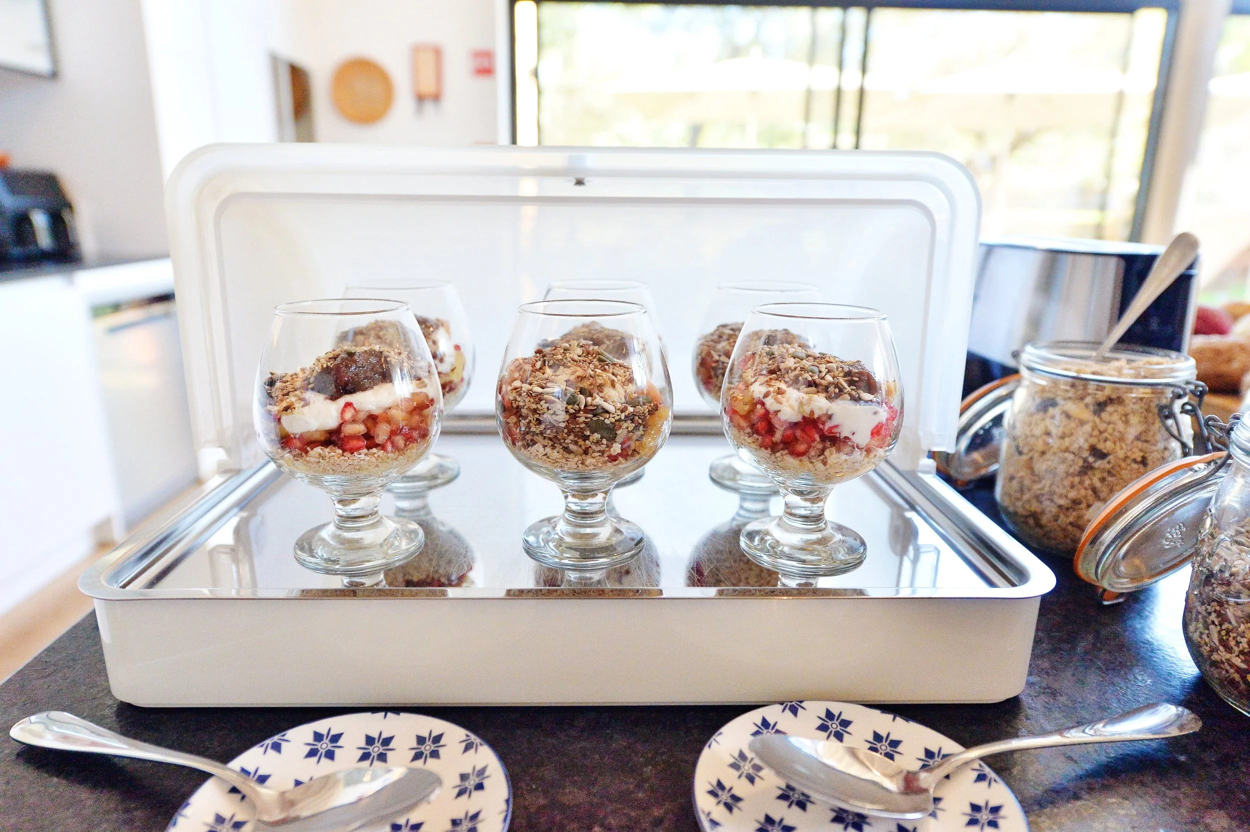 Dessert parfaits in glasses with layered ingredients, served on a tray at a buffet or gathering.
