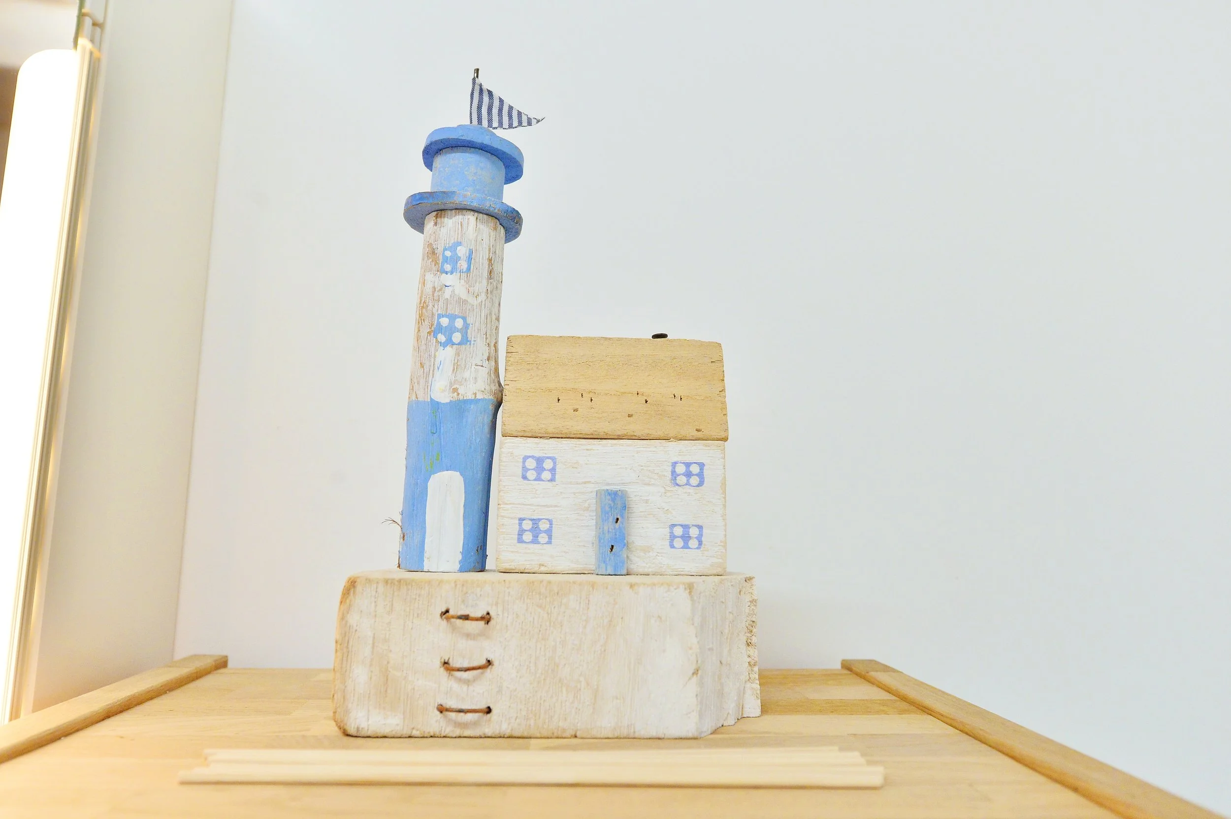 Decorative wooden lighthouse and house toy painted in blue and white, placed on a wooden surface.