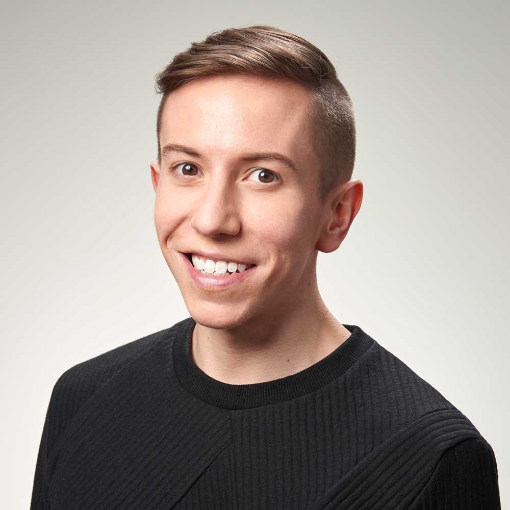 A young man with short brown hair smiling wearing a black shirt against a plain light background.