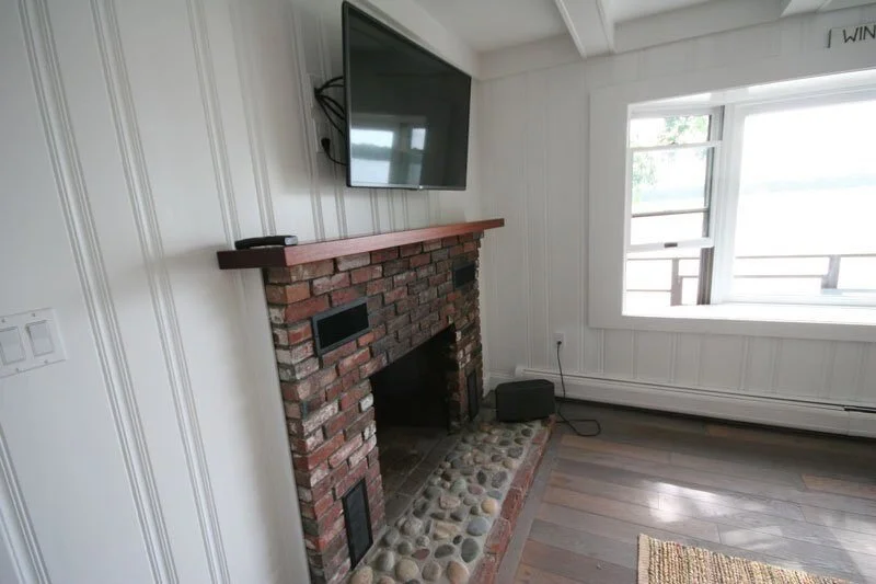 Restored brick fireplace with TV in a Mashpee lakefront cottage, part of a remodel by At Design Remodel.jpg