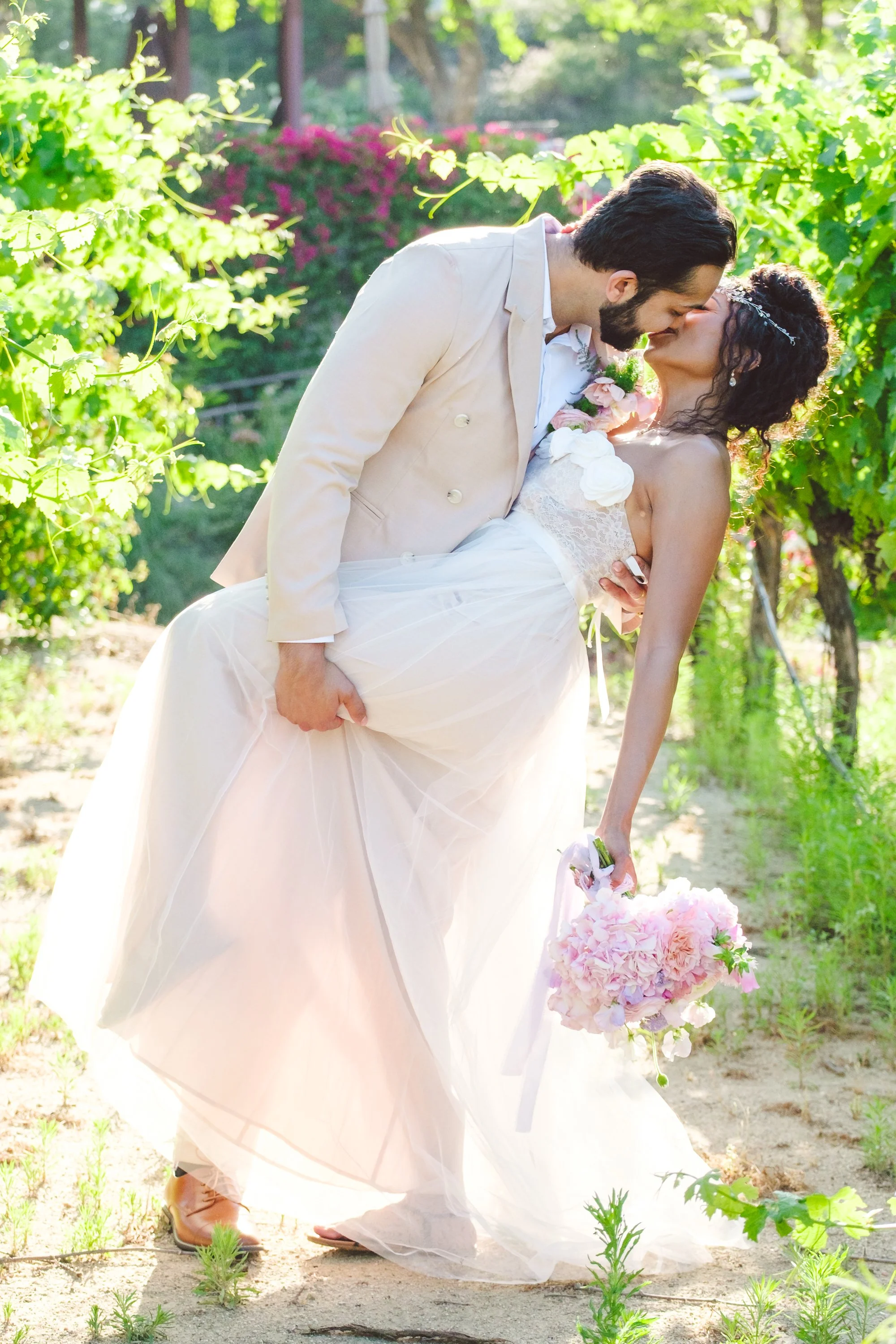 Bride and groom sharing a playful dip kiss among vineyard greenery at the Inn at Churon Winery in Temecula, CA.