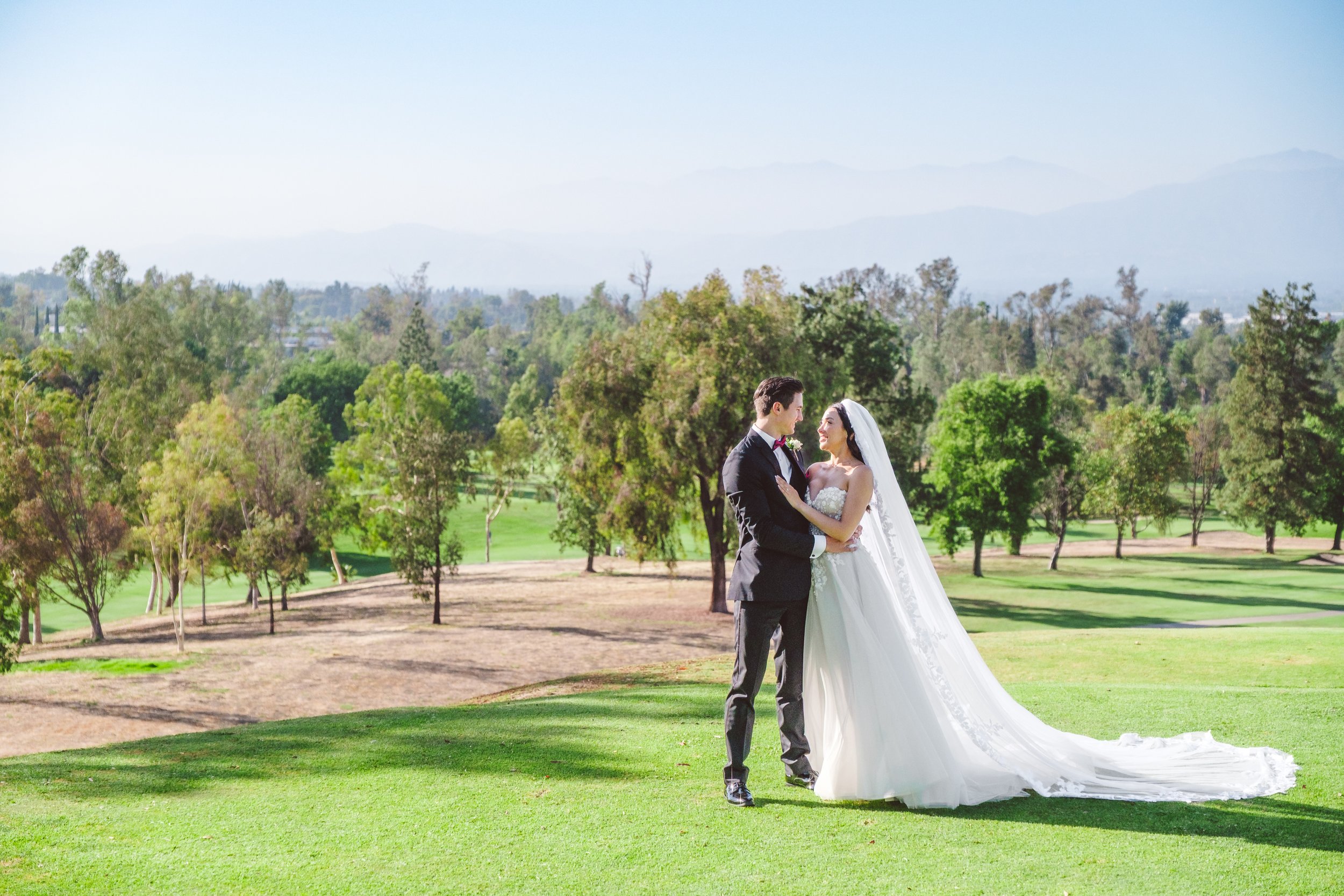 Bride and groom embracing on the golf course at Los Serranos Country Club with rolling hills in the background, Chino Hills CA wedding photography.