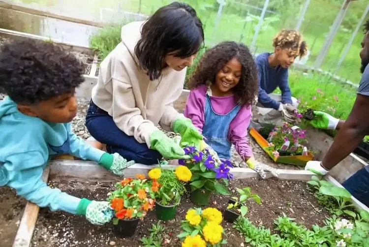 Adults helping kids plant flowers in a garden bed.