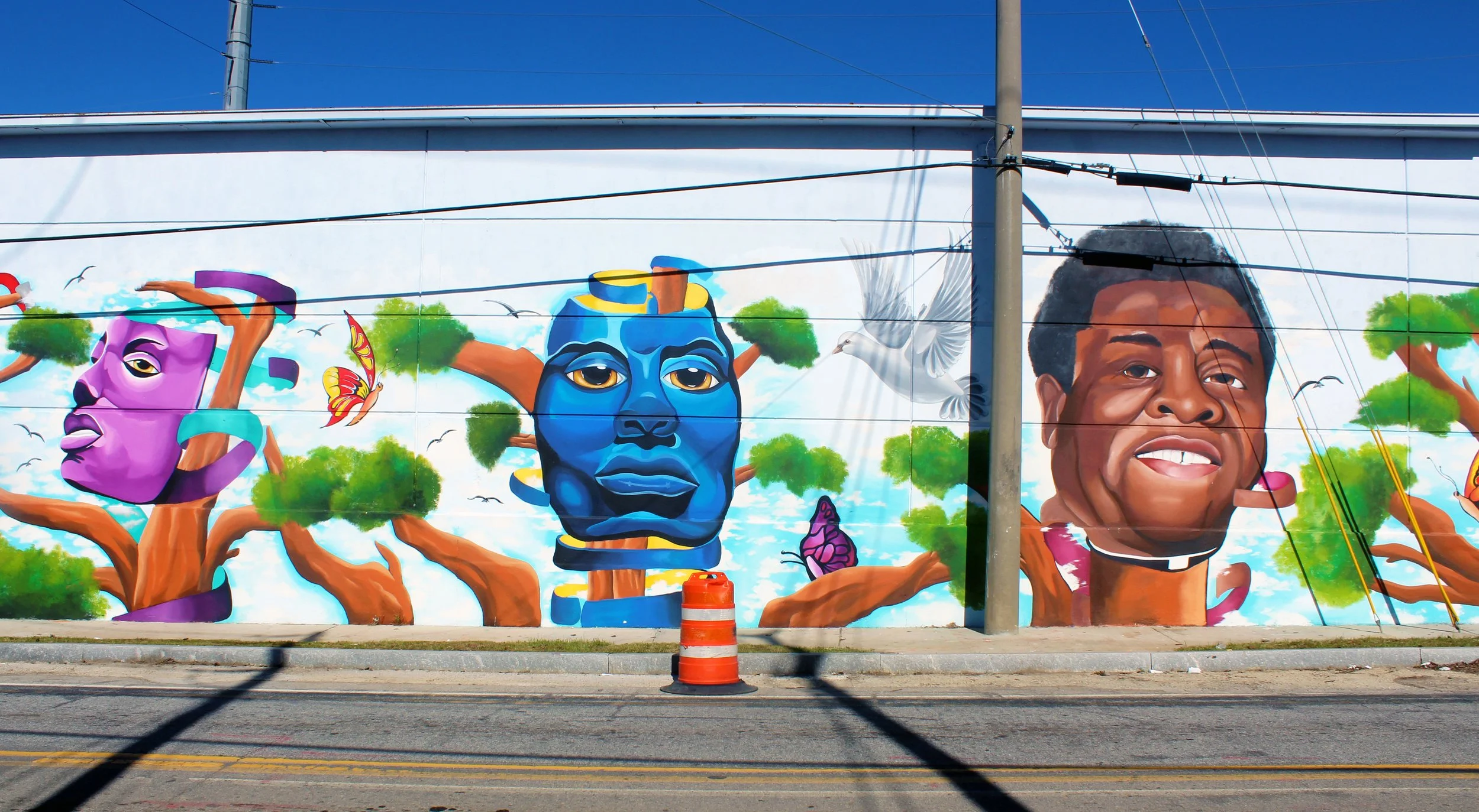 Colorful mural on a wall featuring stylized portraits of people with artistic elements like trees, birds, and butterflies.