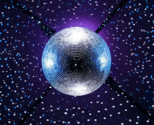 A disco ball reflecting light against a dark background with small, colorful light spots.