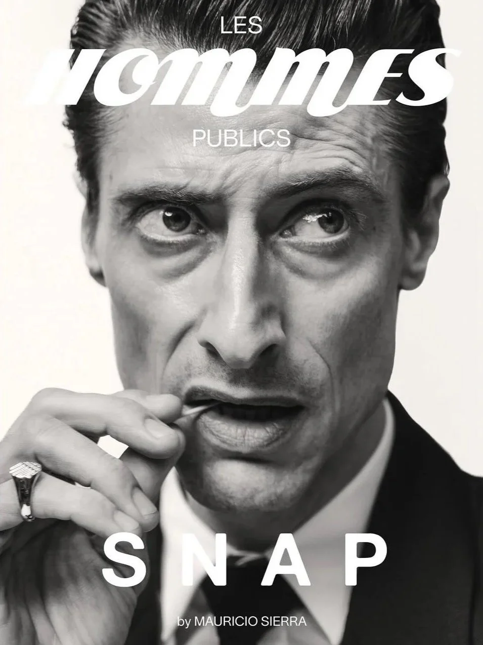 Black and white photo of a man with slicked-back hair, wearing a tuxedo, holding a cigarette near his mouth, with text overlay reading 'Les Hommes Pubics Snap by Mauricio Sierra'.