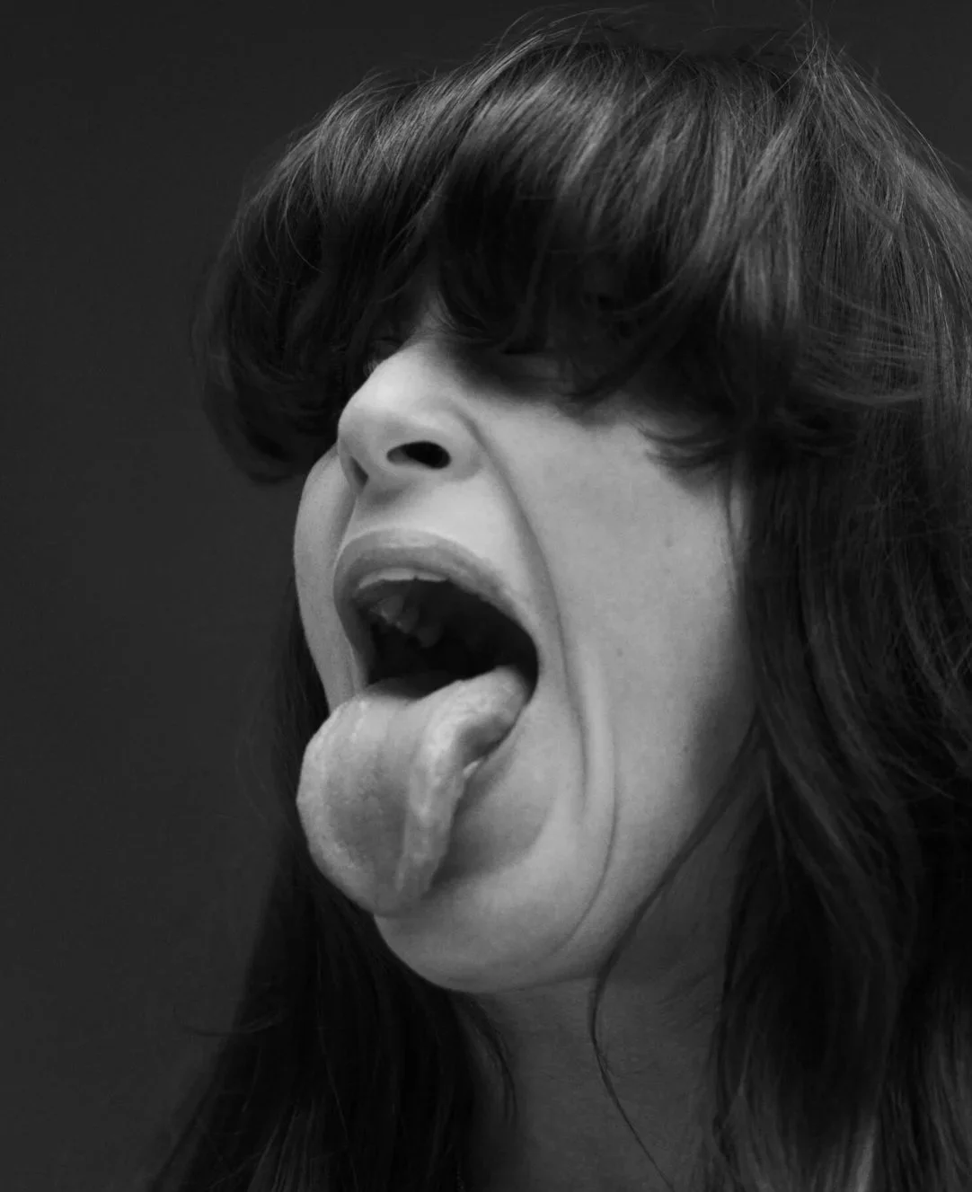 Black and white close-up of a woman with her hair covering part of her face, mouth open with tongue sticking out.