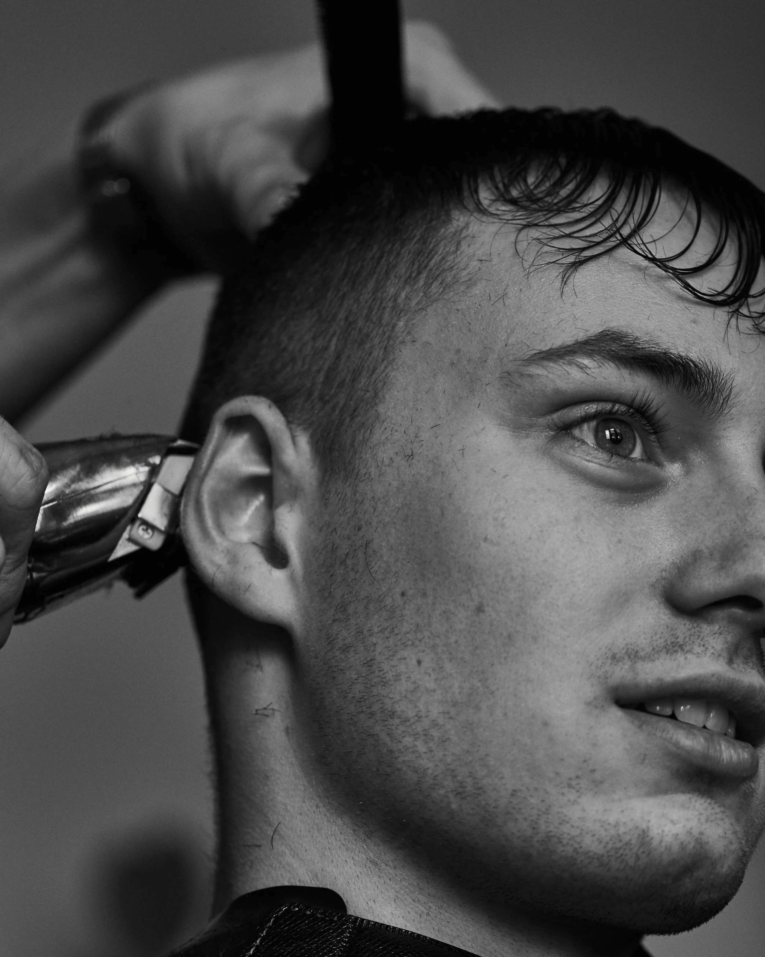 A man getting a haircut at a barbershop, with one side of his head shaved and the other hair being cut.