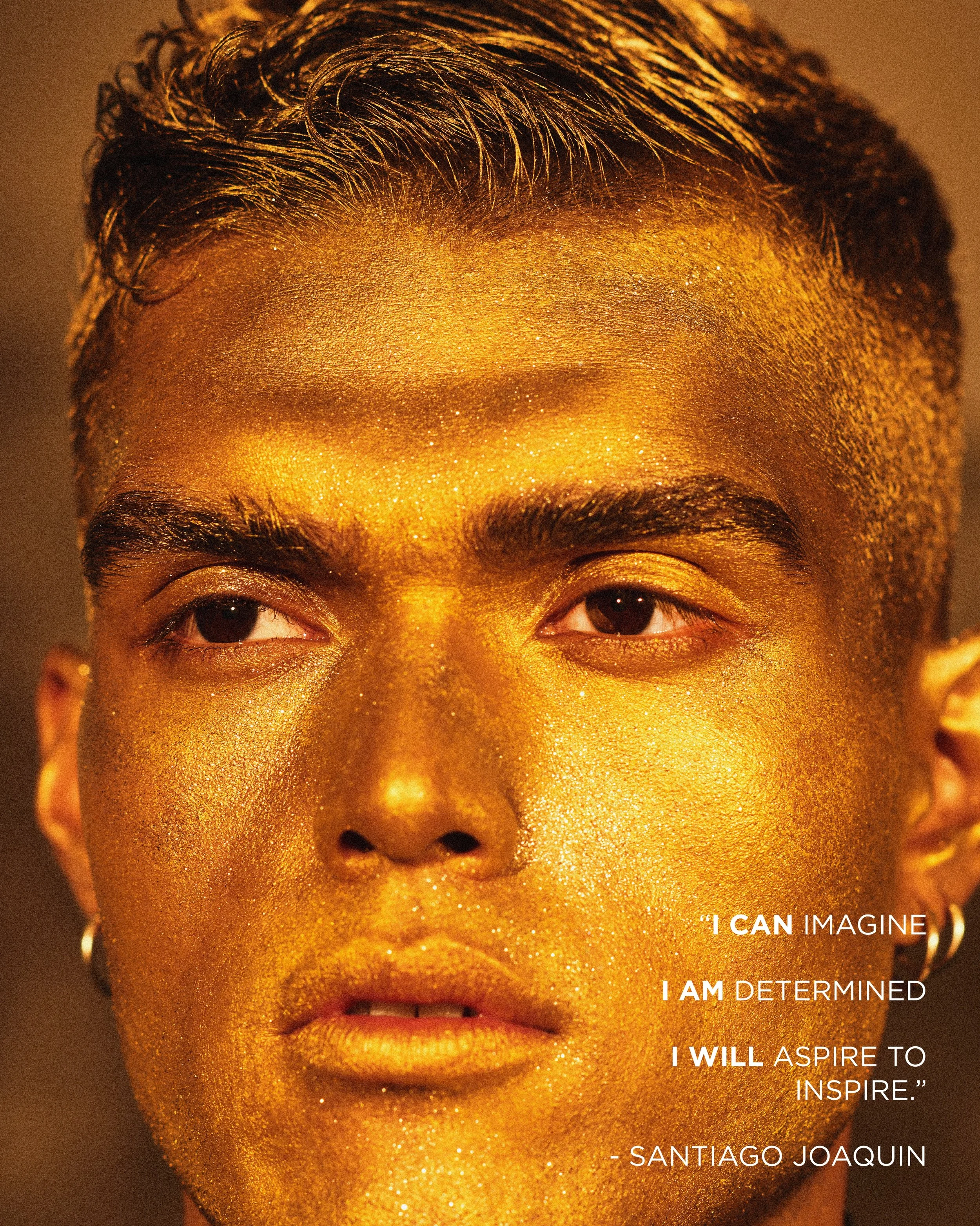 Close-up of a person with short, dark hair and gold glitter makeup on their face, with a quote by Santiago Joaquin that reads, 'I CAN IMAGINE, I AM DETERMINED, I WILL ASPIRE TO INSPIRE.'