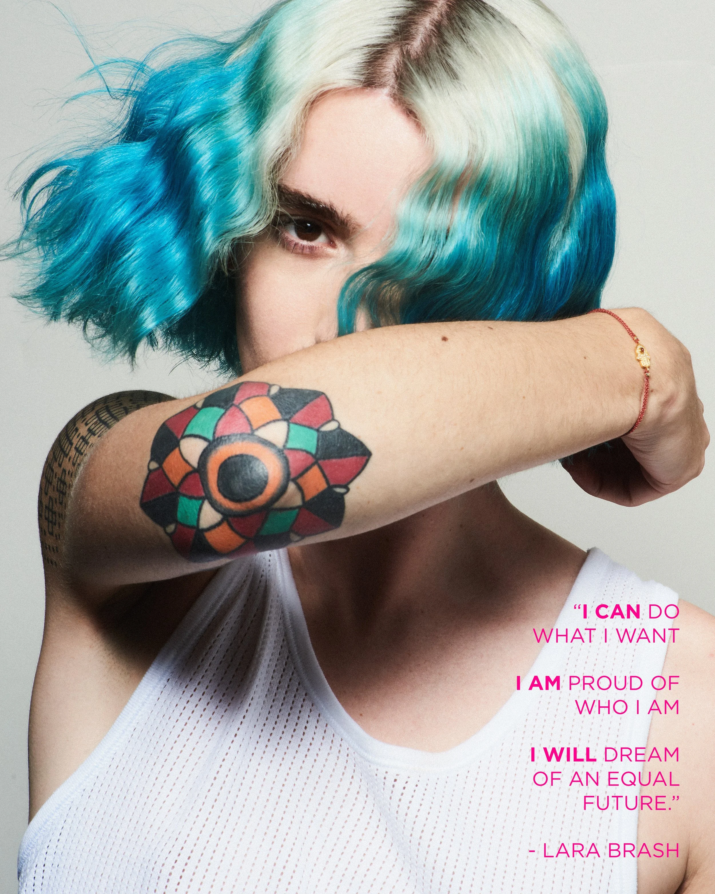 A woman with blue, green, and platinum hair partially covering her face, showing an arm tattoo and a white tank top, with an inspirational quote by Lara Brash in pink text.