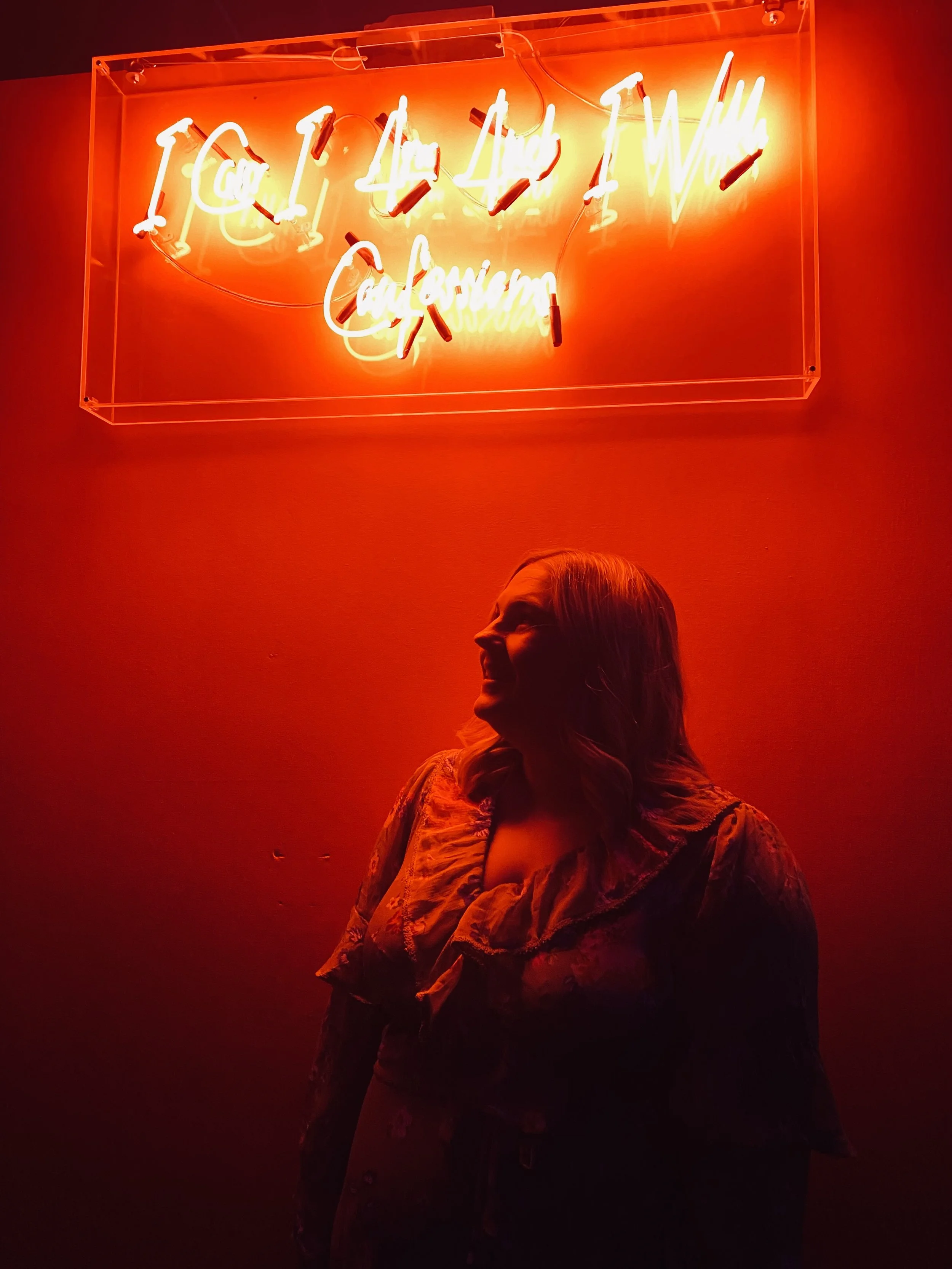 A person standing in front of a neon sign that says, "I'll kill you if I will, go crazy or not," on a red-colored wall.