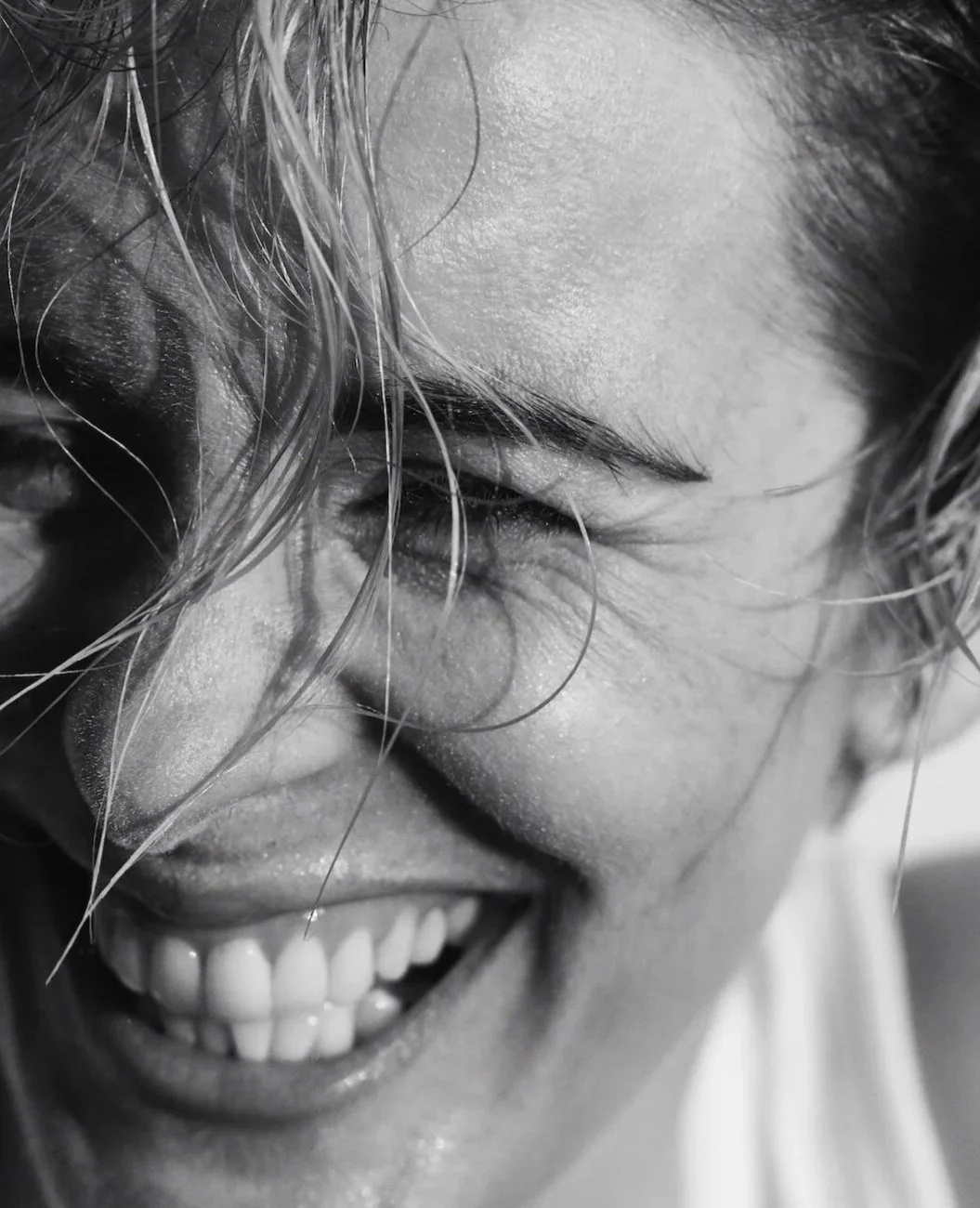 Close-up of a smiling person with wet hair, showing their teeth, with a focus on their face and smile.