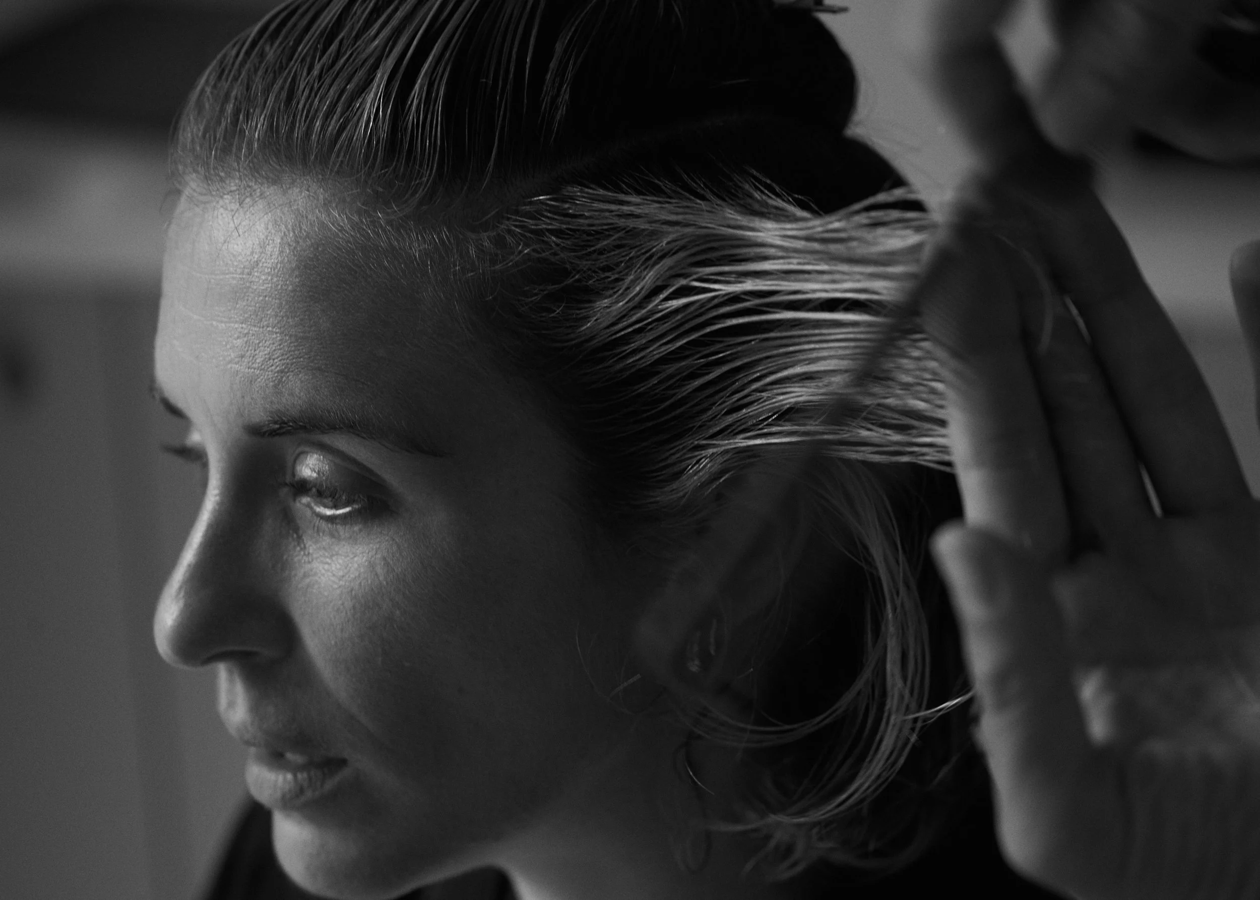 A woman is getting her hair washed or styled at a salon, with her eyes closed and hand touching her hair.