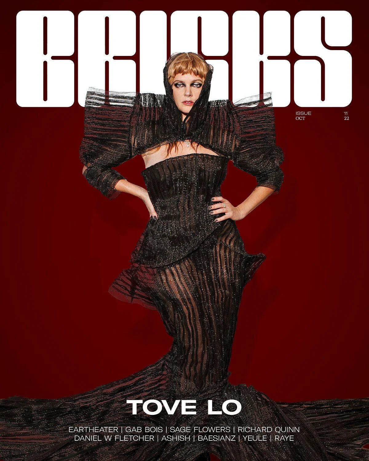 Tove Lo on the cover of a magazine, wearing a black, shimmering, striped gown with dramatic shoulders and a high slit, posed against a deep red background.