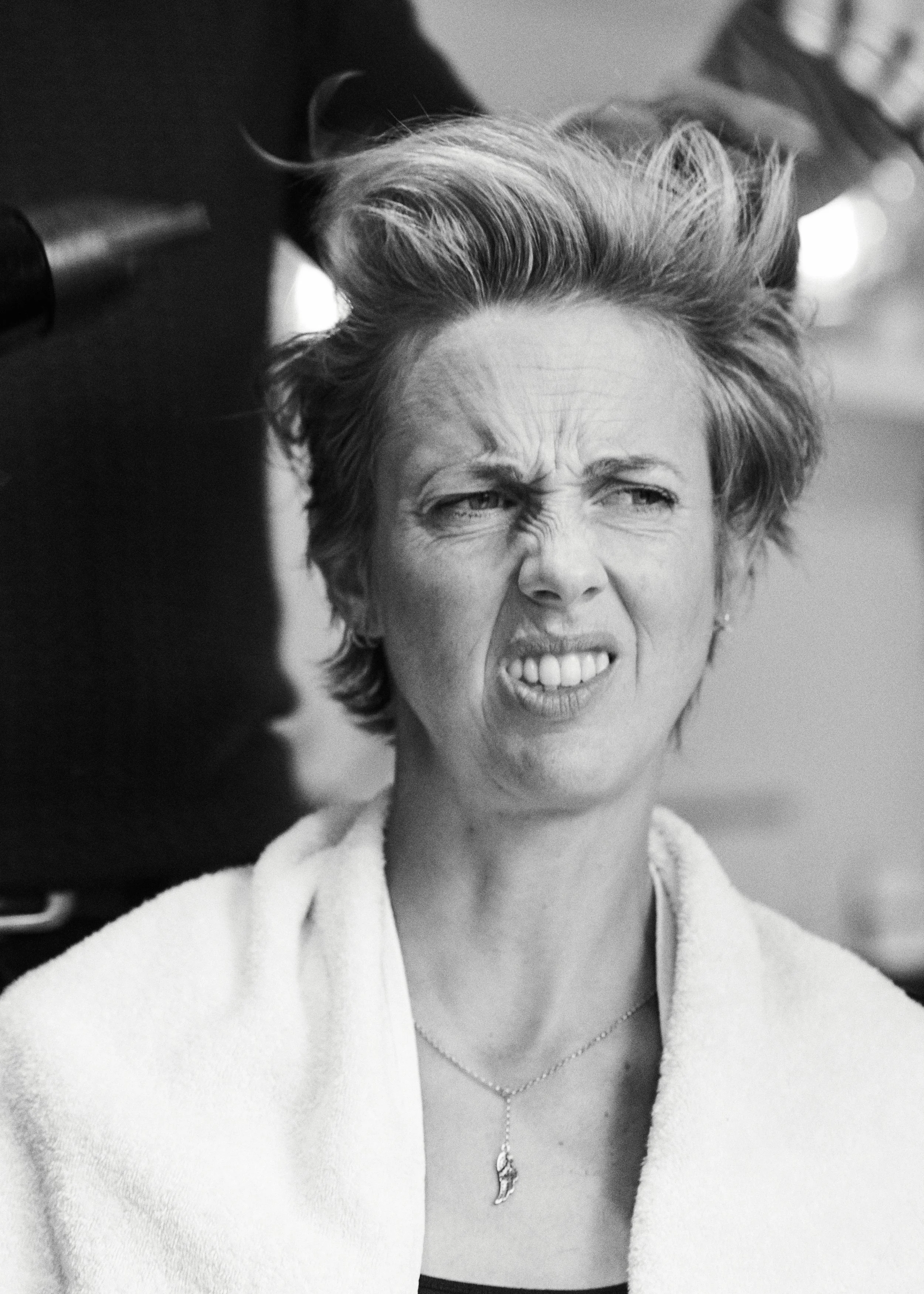 A woman with short, styled hair getting her hair done at a salon, making a funny facial expression.