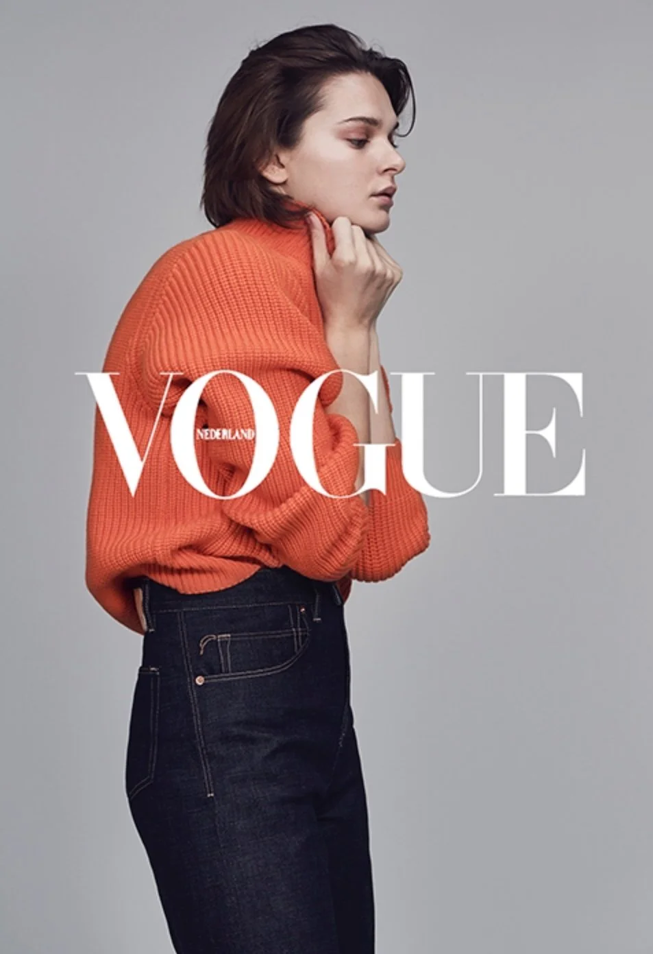 Side profile of a woman with brown hair wearing an orange sweater, standing against a gray background, with 'VOGUE NEDERLAND' written across the image.
