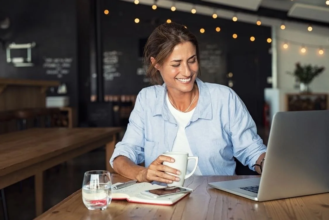 Vrouw glimlacht achter laptop met koffie, symbool voor persoonlijke e-mailcoaching op maat.
