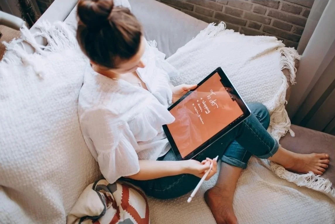 een vrouw op haar bank, werkt op een ipad aan haar emailcoaching