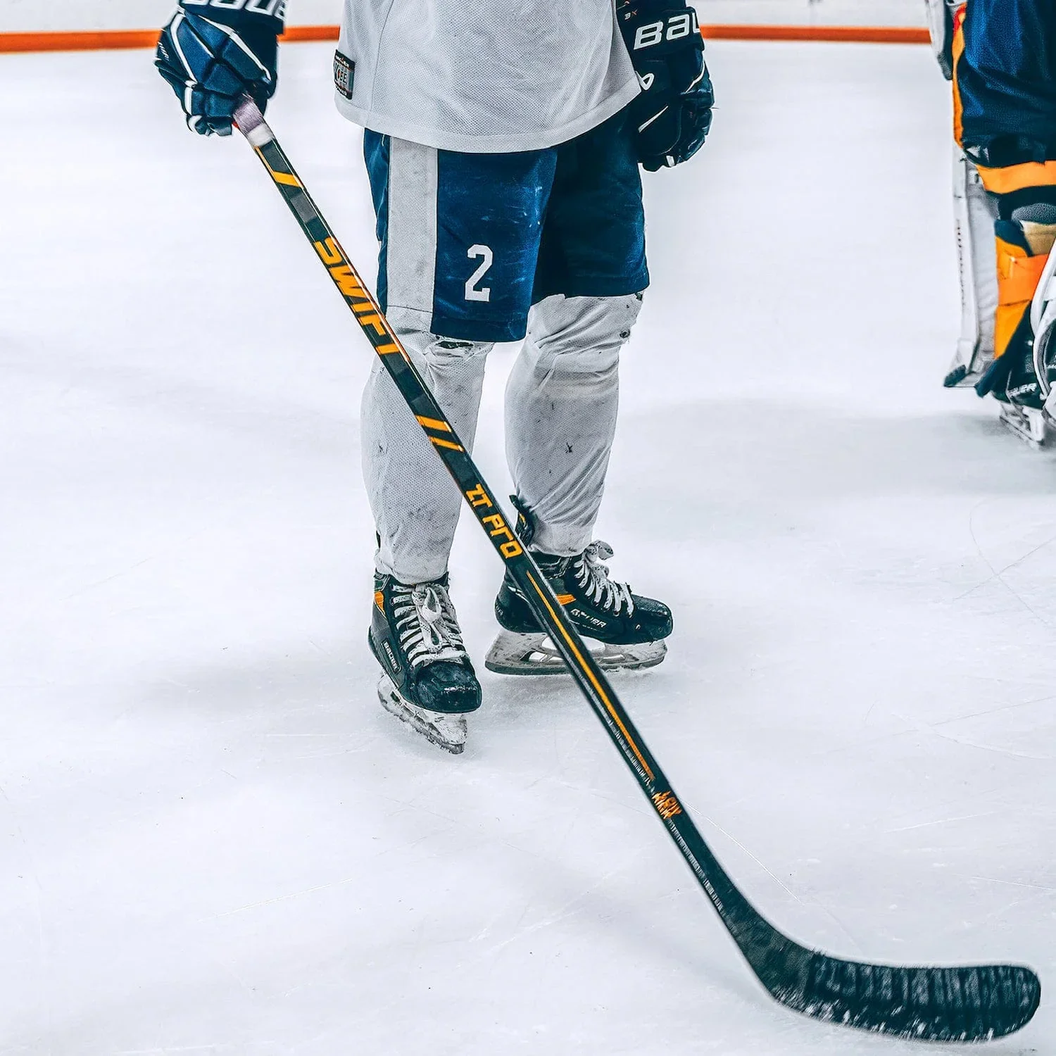 Joueur de hockey sur glace en équipement, debout sur la glace, tenant une crosse de hockey.